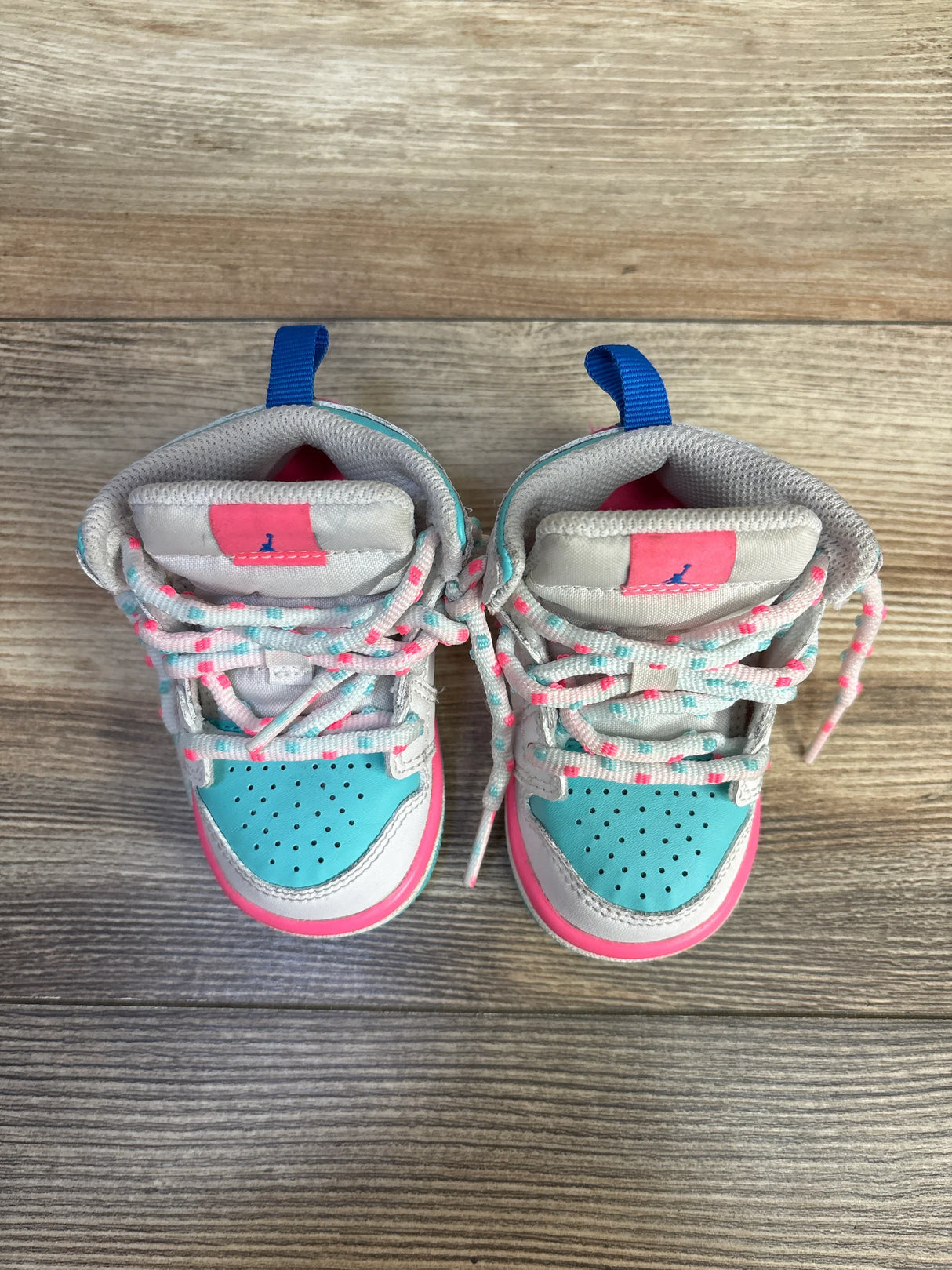 Aqua and pink baby sneakers with blue pull tabs on wood floor
