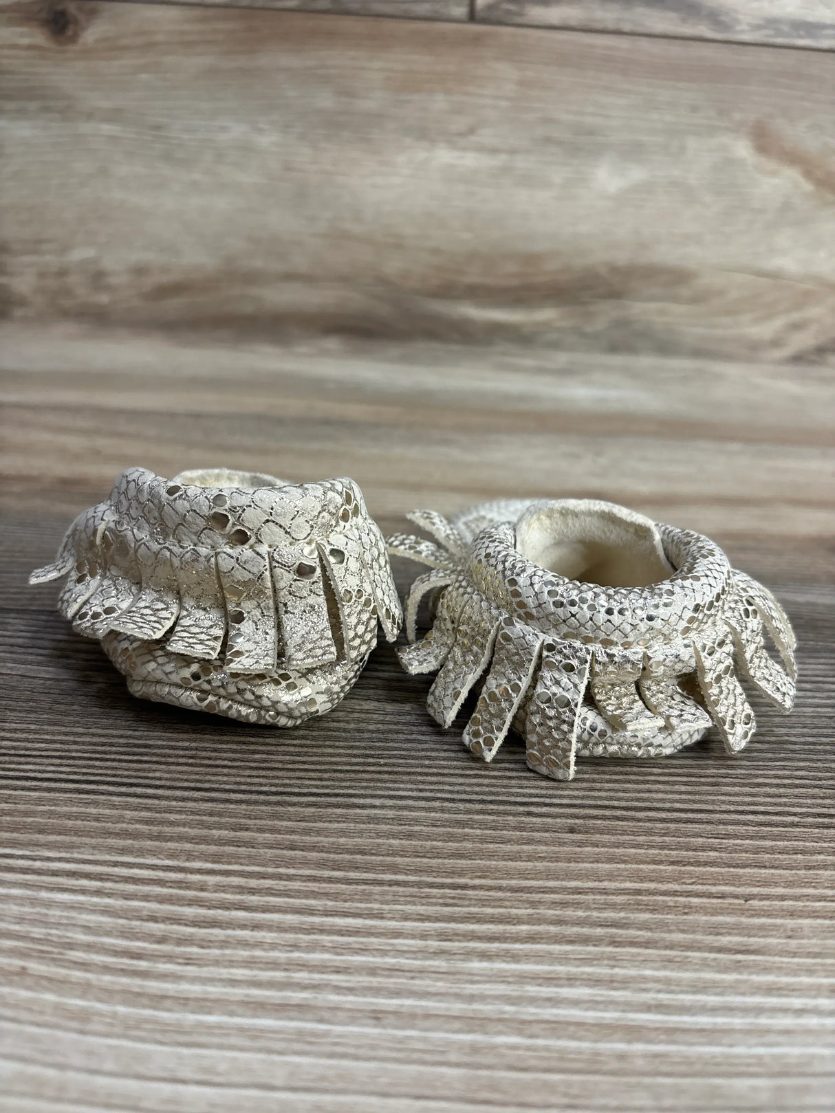 Pair of cream-colored baby moccasins with textured fringe, displayed on wooden surface for kids resale