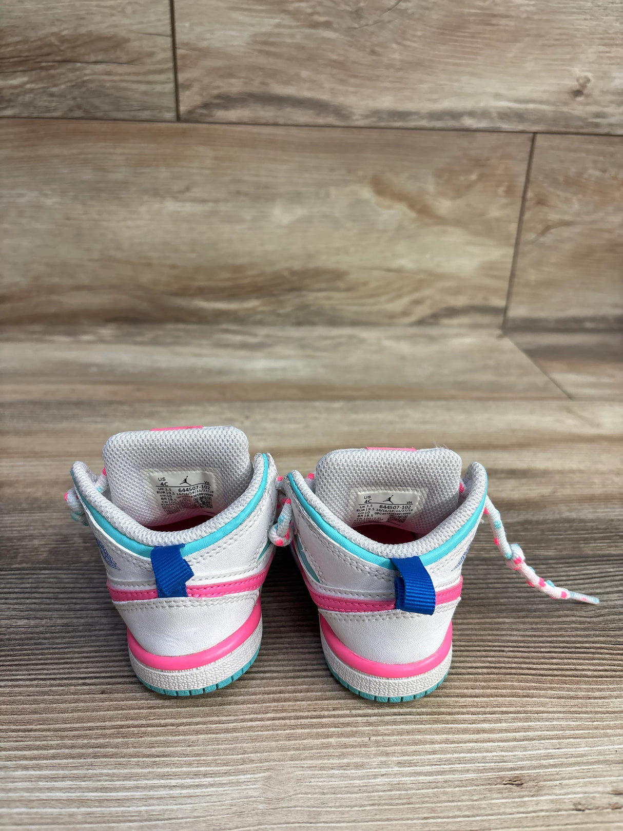 Back view of white toddler sneakers with pink and teal accents on wood floor