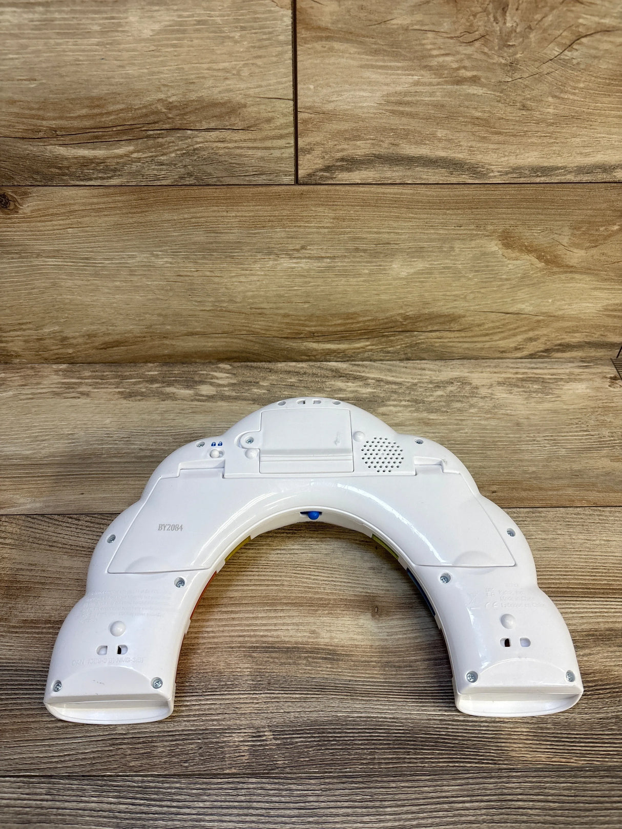 Back of Baby Einstein Glow and Discover Light Bar, curved white housing with battery compartment and speaker on wood floor