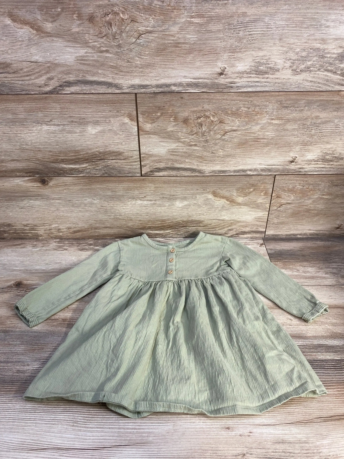 Flat lay of Cat & Jack green long-sleeve henley dress showcasing gathered skirt and three wooden buttons on light wood background