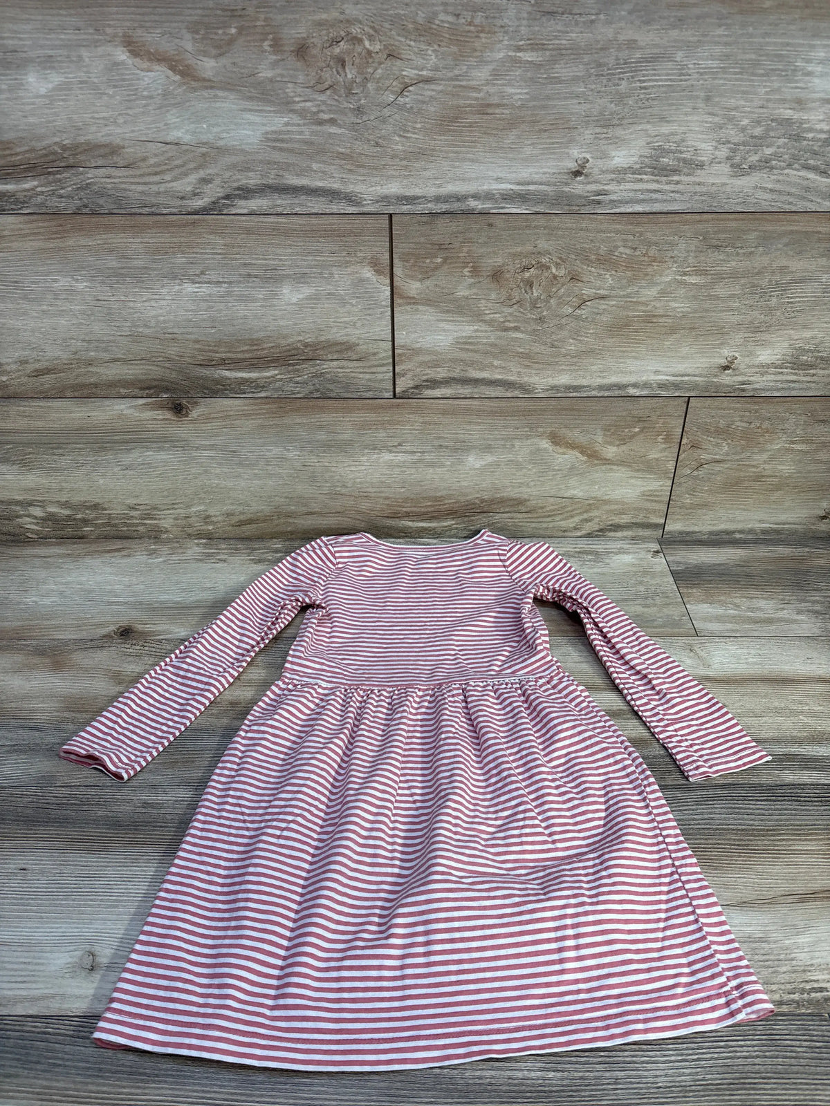 Front view of Carter’s pink and white striped long-sleeve dress with a gathered waist and full skirt on a wood-look floor