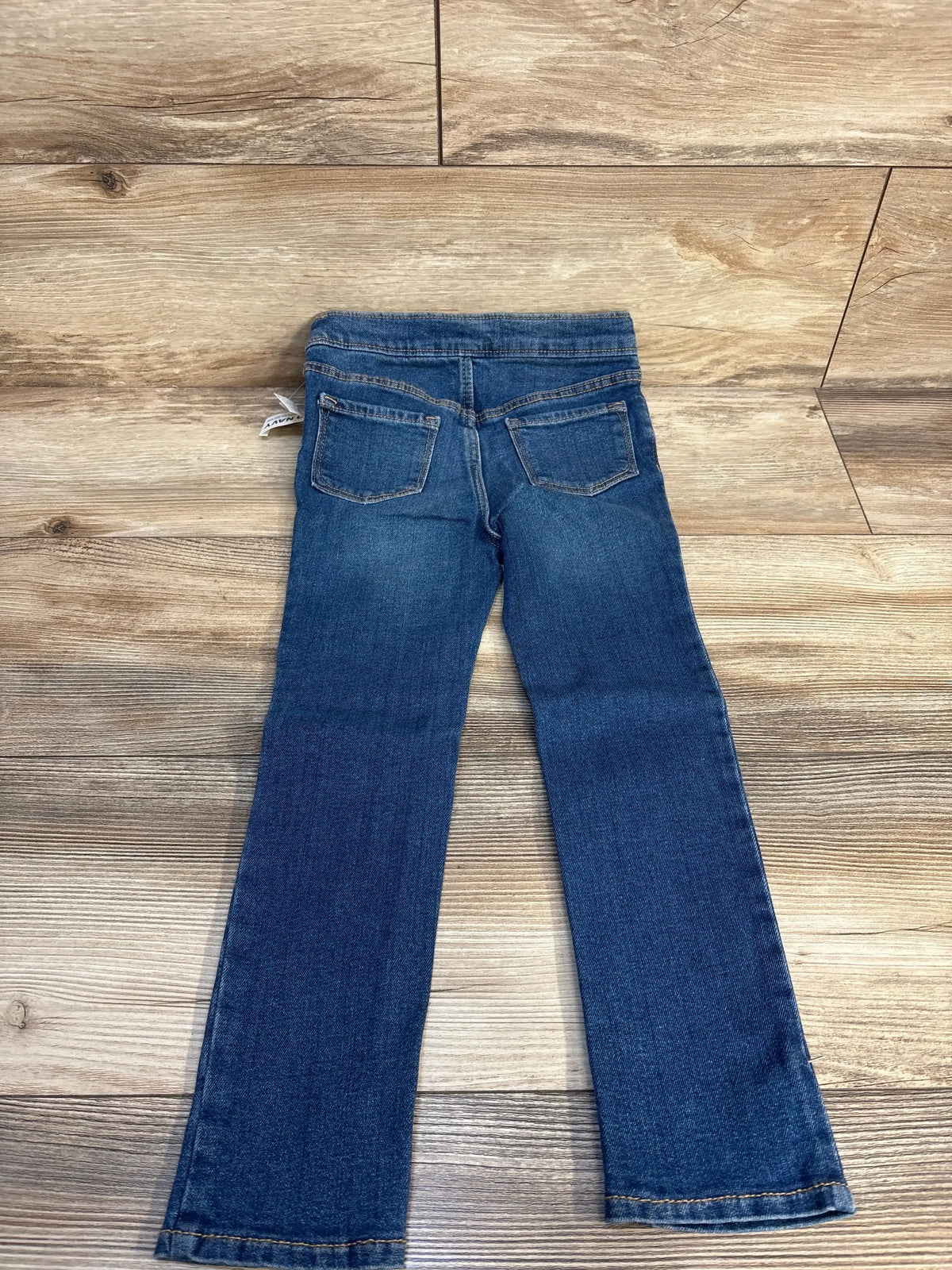 Back view of kids blue denim jeans with pockets on wood floor, children's clothing resale