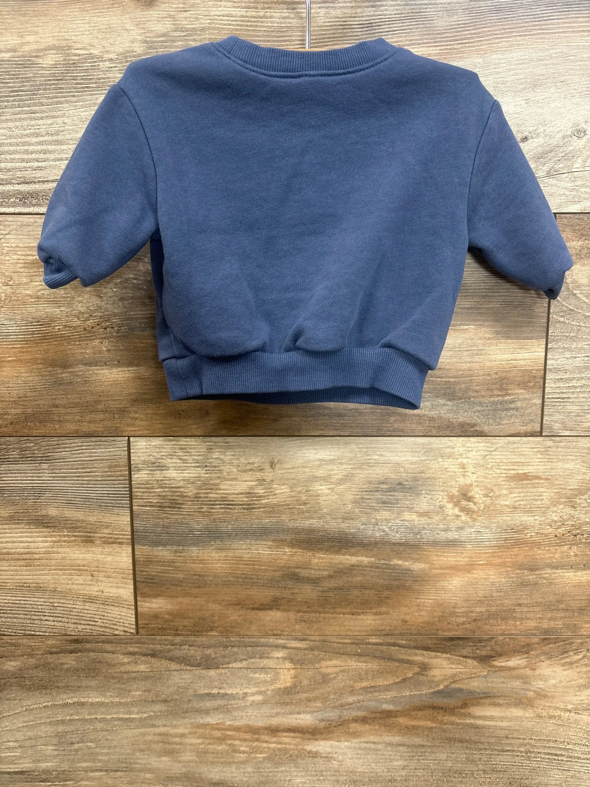 Back view of Old Navy Cute To The Core sweatshirt in blue showing ribbed collar, cuffs, and hem on a wood-grain background