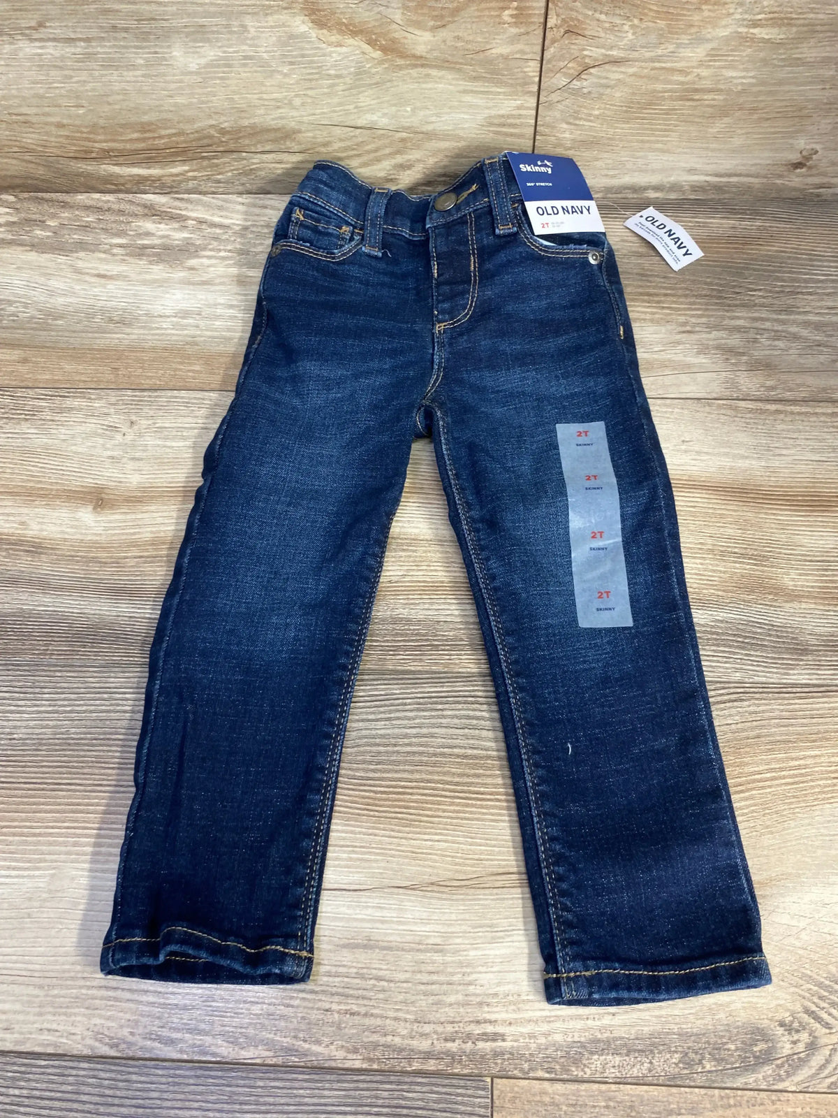 Flat lay of new Old Navy 360 Stretch skinny jeans in dark wash size 2T with hangtags on wood plank floor