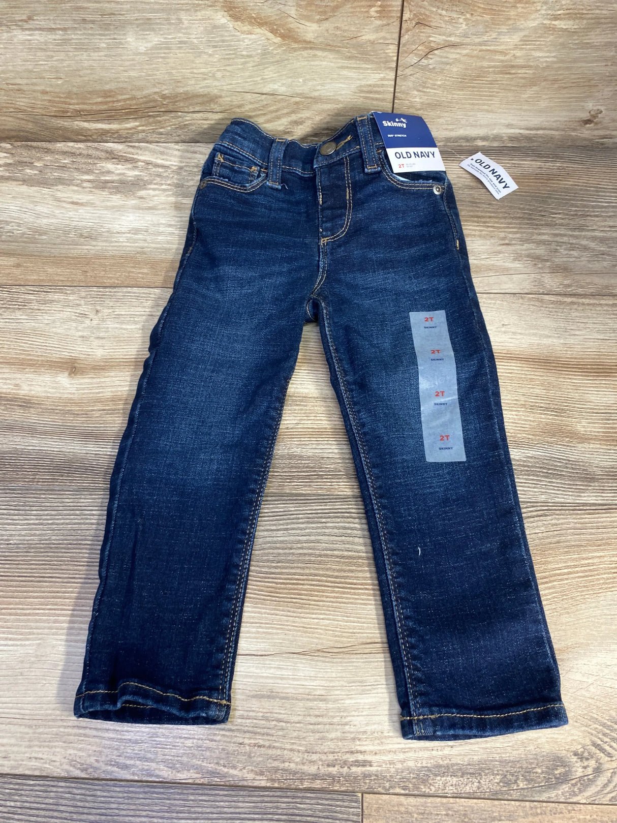 Flat lay of new Old Navy 360 Stretch skinny jeans in dark wash size 2T with hangtags on wood plank floor
