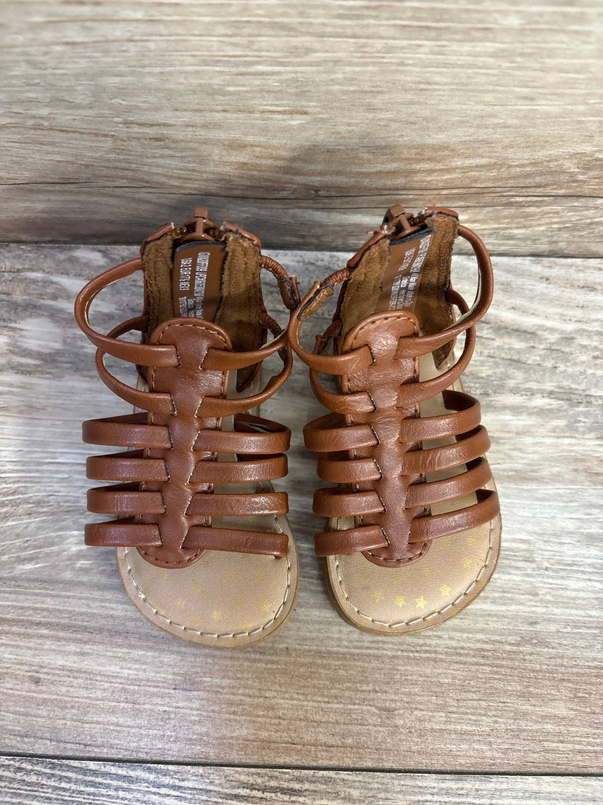 Top-down view of Wonder Nation brown gladiator sandals with multiple leather straps and back zipper on wood background