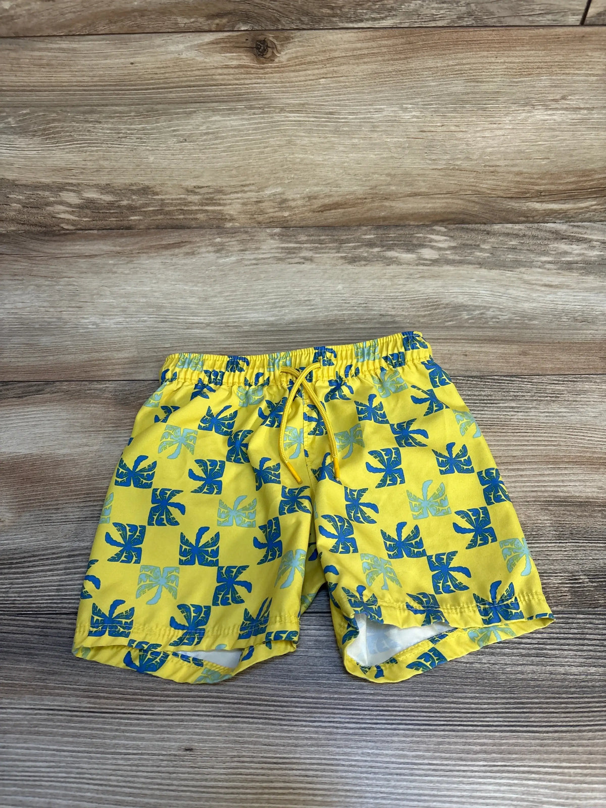 Yellow kids swim trunks with blue tropical leaf print on wood background