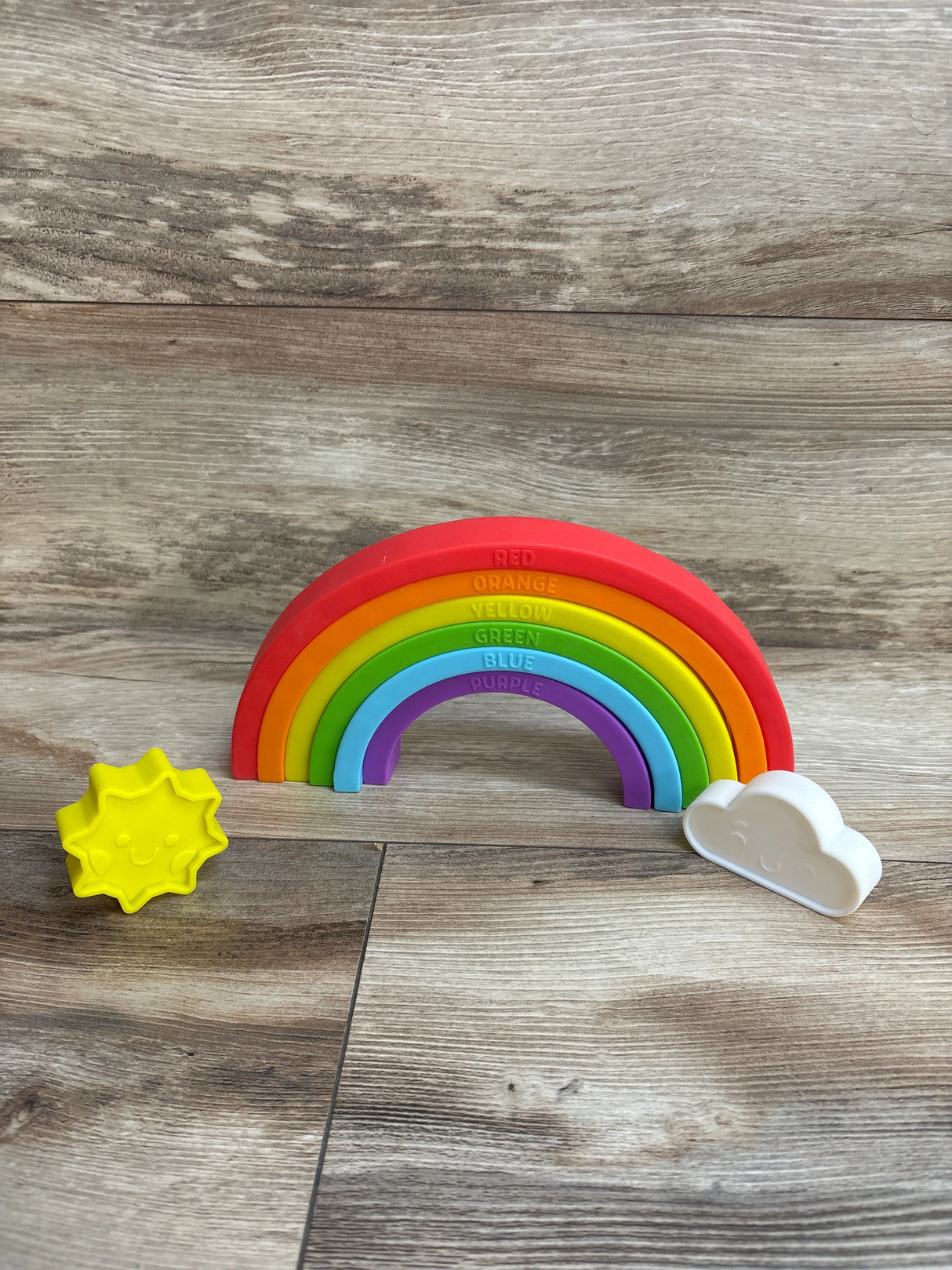 Colorful silicone rainbow toy with yellow sun and white cloud on wood background