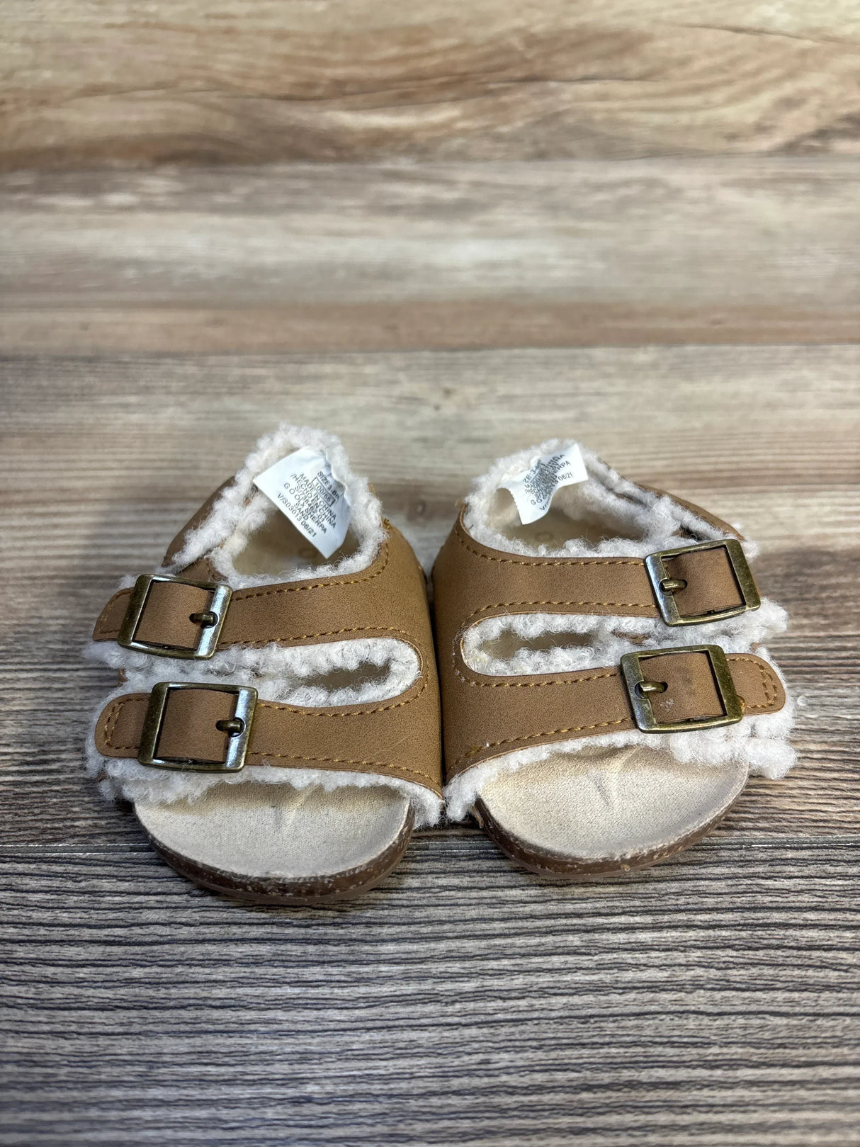 Front view of Old Navy sherpa-lined baby sandals size 1/2C showing double buckle straps on wood