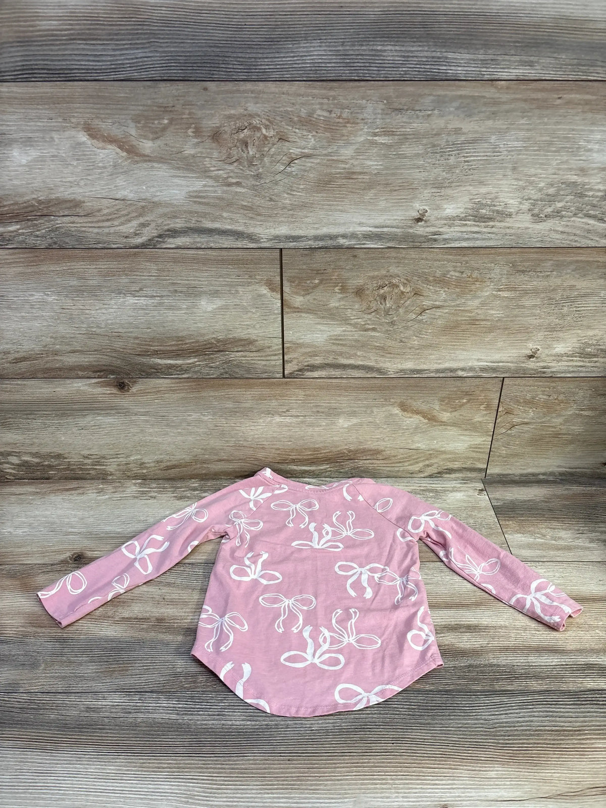 Front view of Cat & Jack pink bow print long sleeve shirt in size 3T showcasing curved hem on wood background