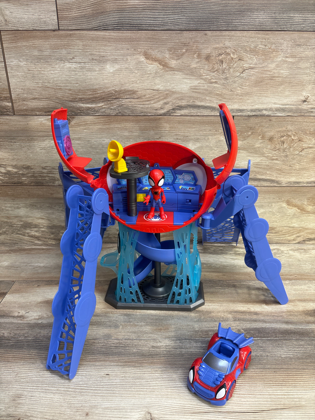 Front view of Spidey Web-Quarters playset with open red and blue hub, Spider-Man figure, and toy car on wood floor