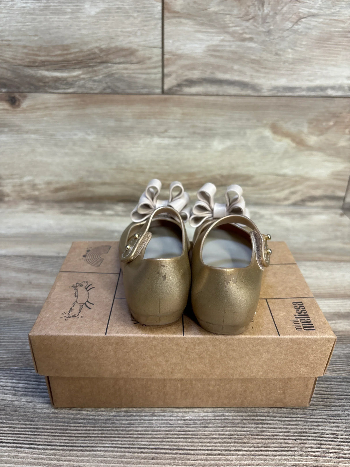 Gold toddler shoes with cream bows on a cardboard box, kids footwear resale