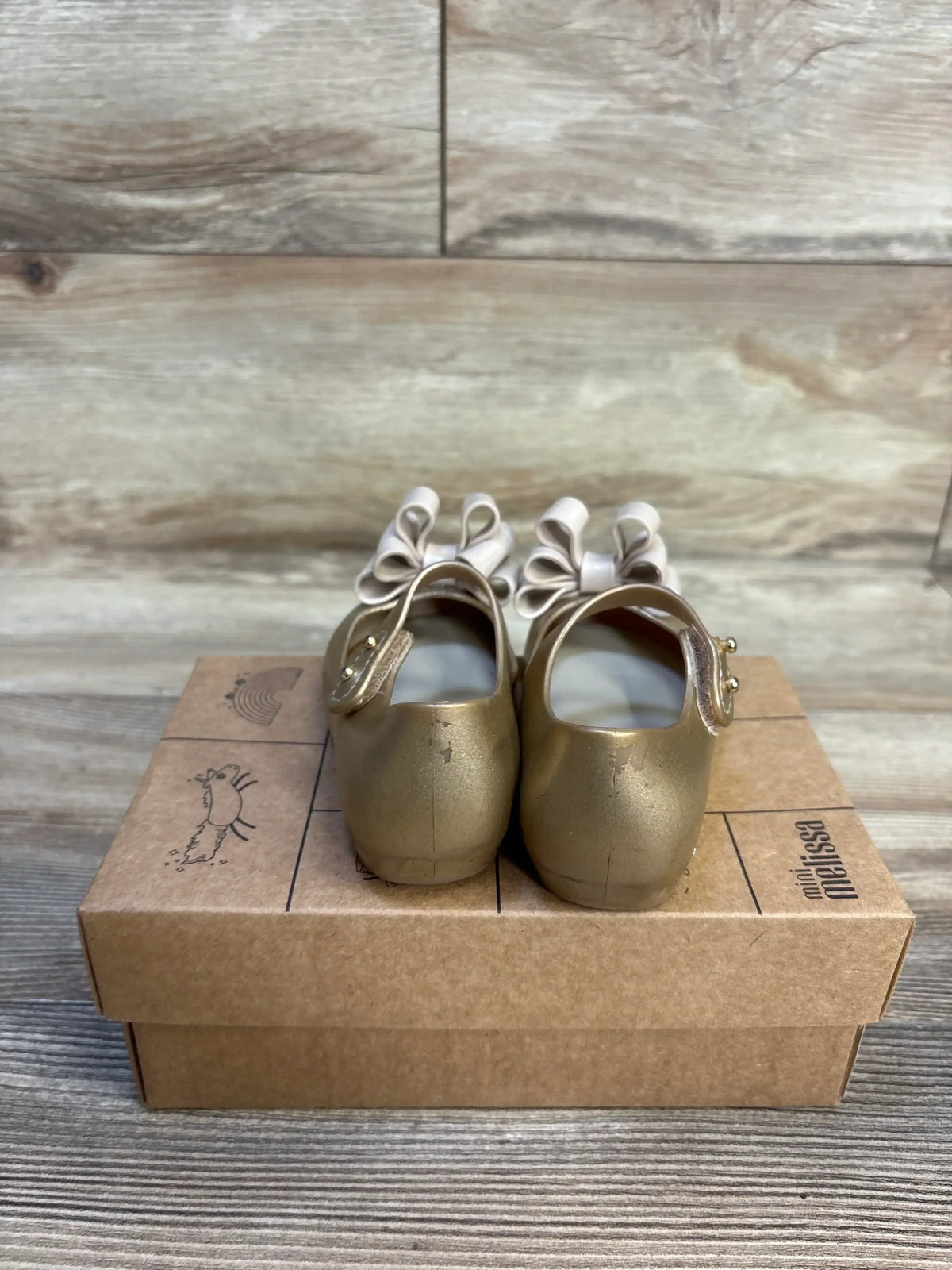 Gold toddler shoes with cream bows on a cardboard box, kids footwear resale