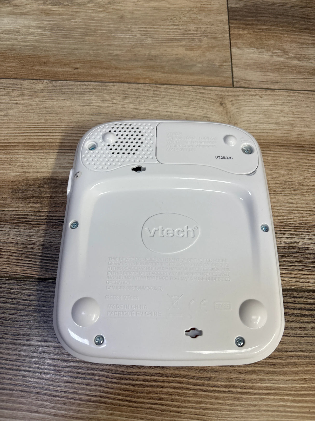 Rear view of VTech Discover & Learn Tablet showcasing battery compartment, speaker grille, embossed VTech logo and keyhole mounting slots on wood floor background