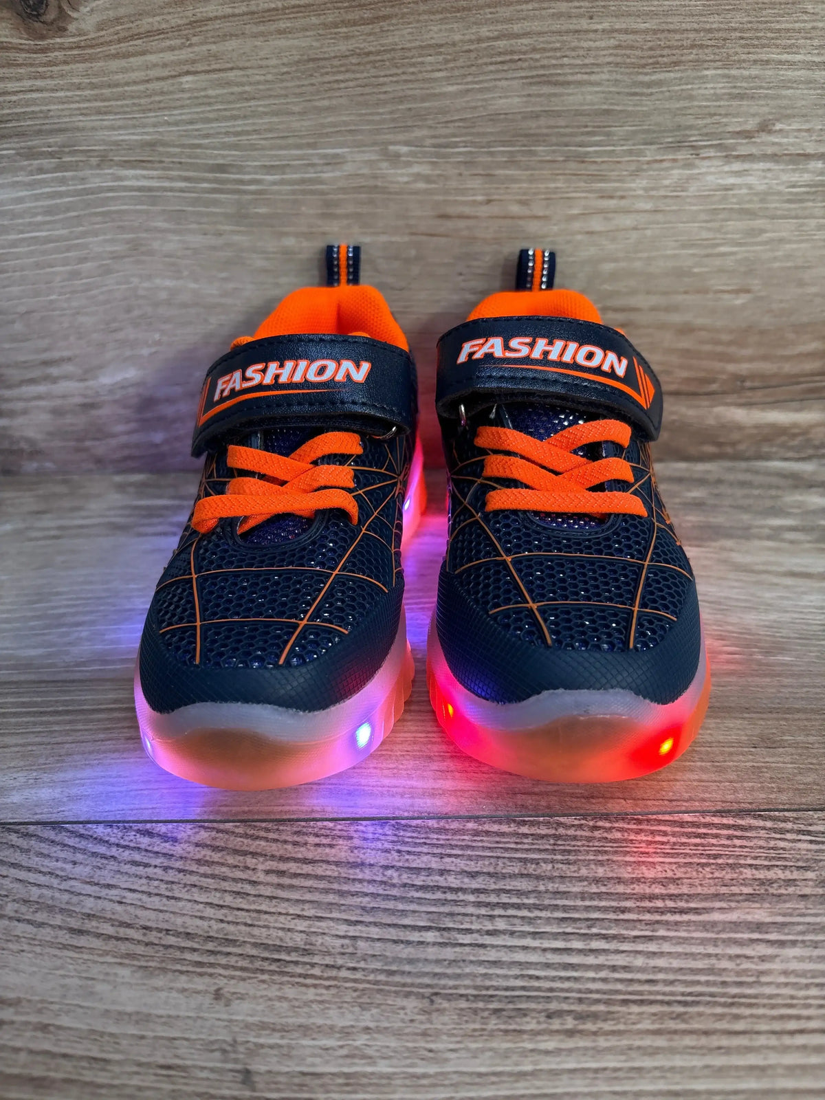 Front view of Jian Dian navy and orange light-up toddler sneakers showcasing glowing multicolor soles on a wood background