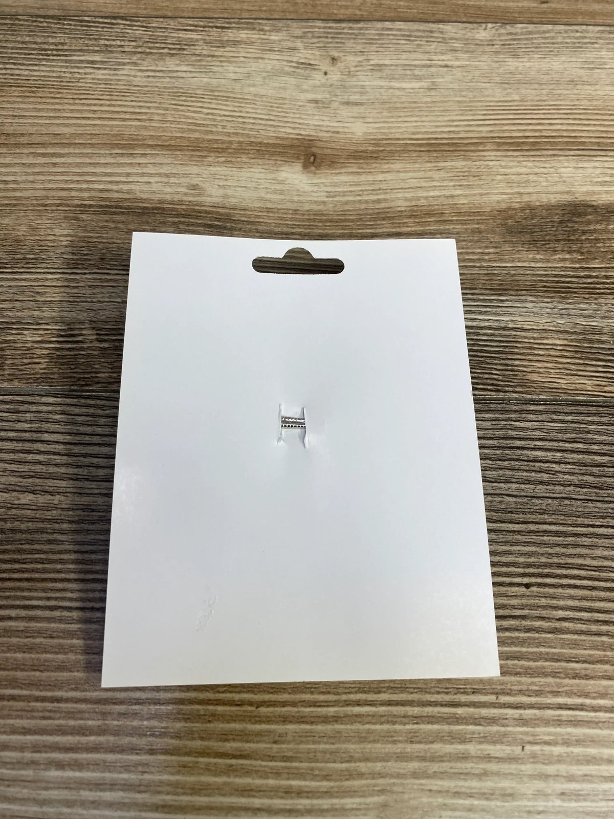 Blank white product tag with hang hole on wood surface, ready for kids or maternity item labeling