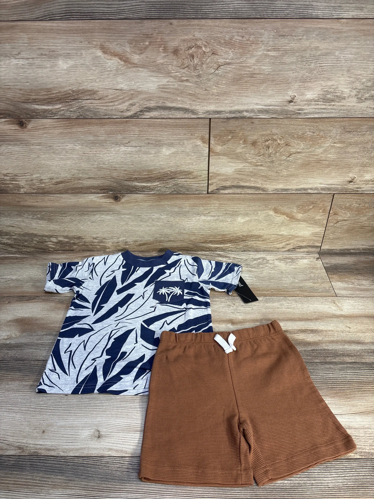 Front view of Picapino two-piece set in size 4T, with a navy patterned shirt and brown ribbed shorts on wood-look background