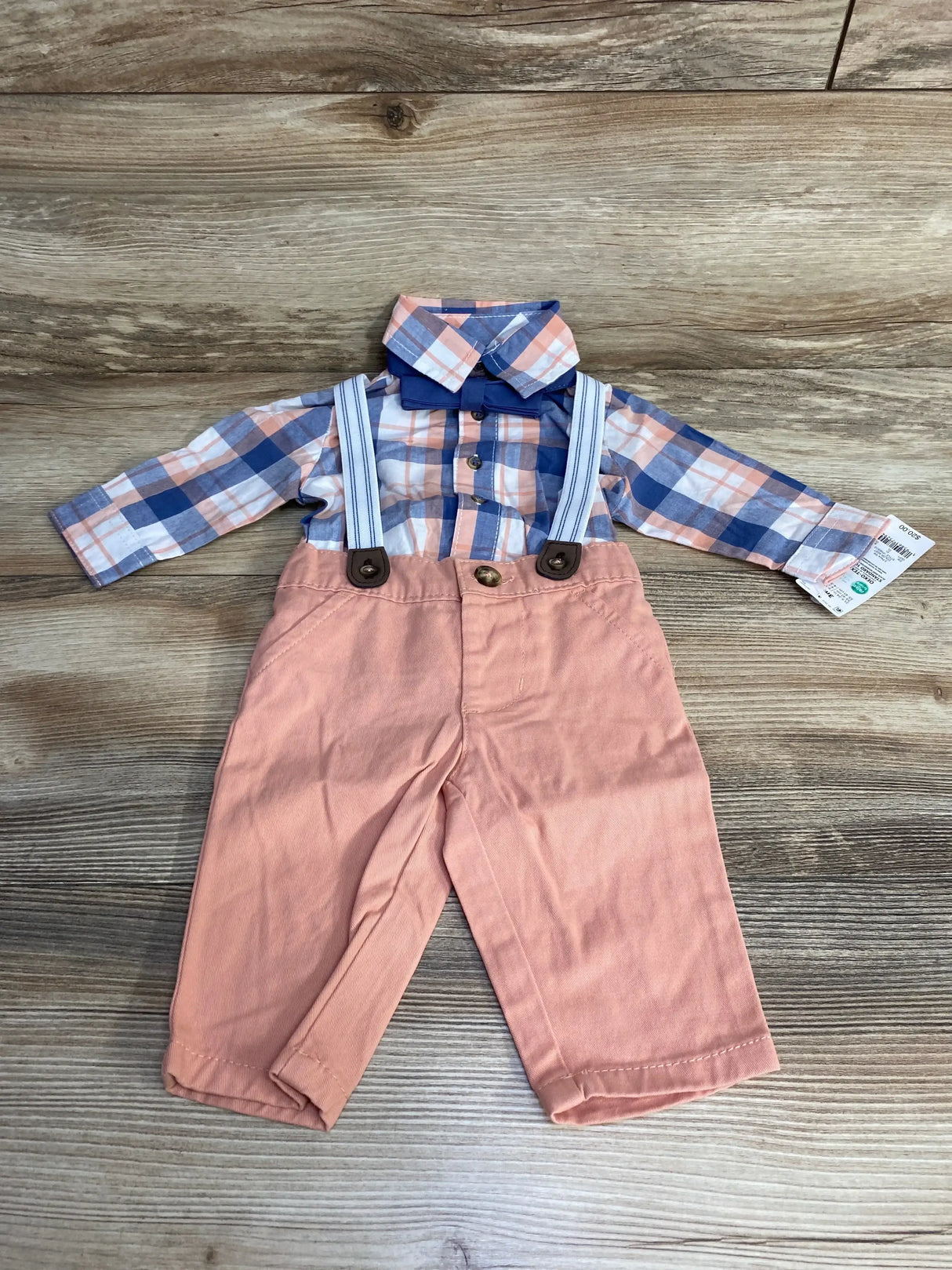 Front flat-lay of baby plaid button-up with navy bow tie and peach suspender pants with striped suspenders on wood background