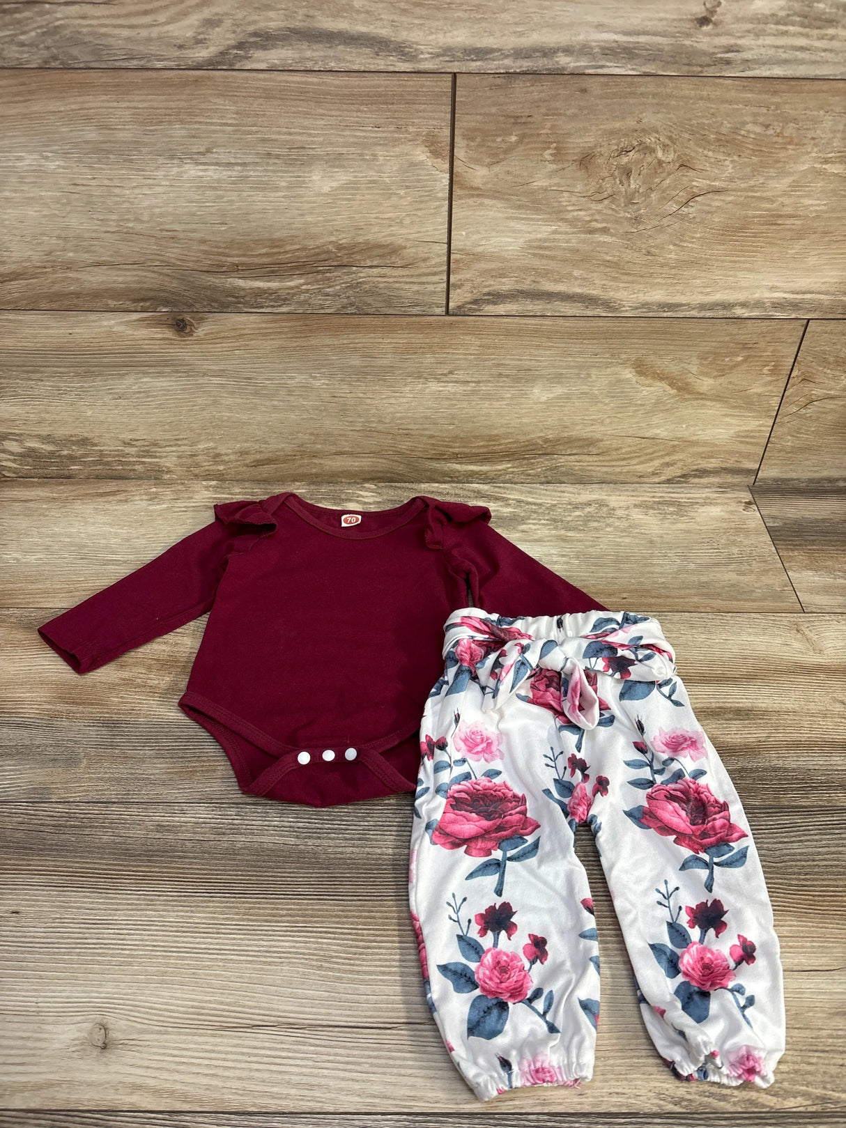 Burgundy baby bodysuit and floral pants set on wood background