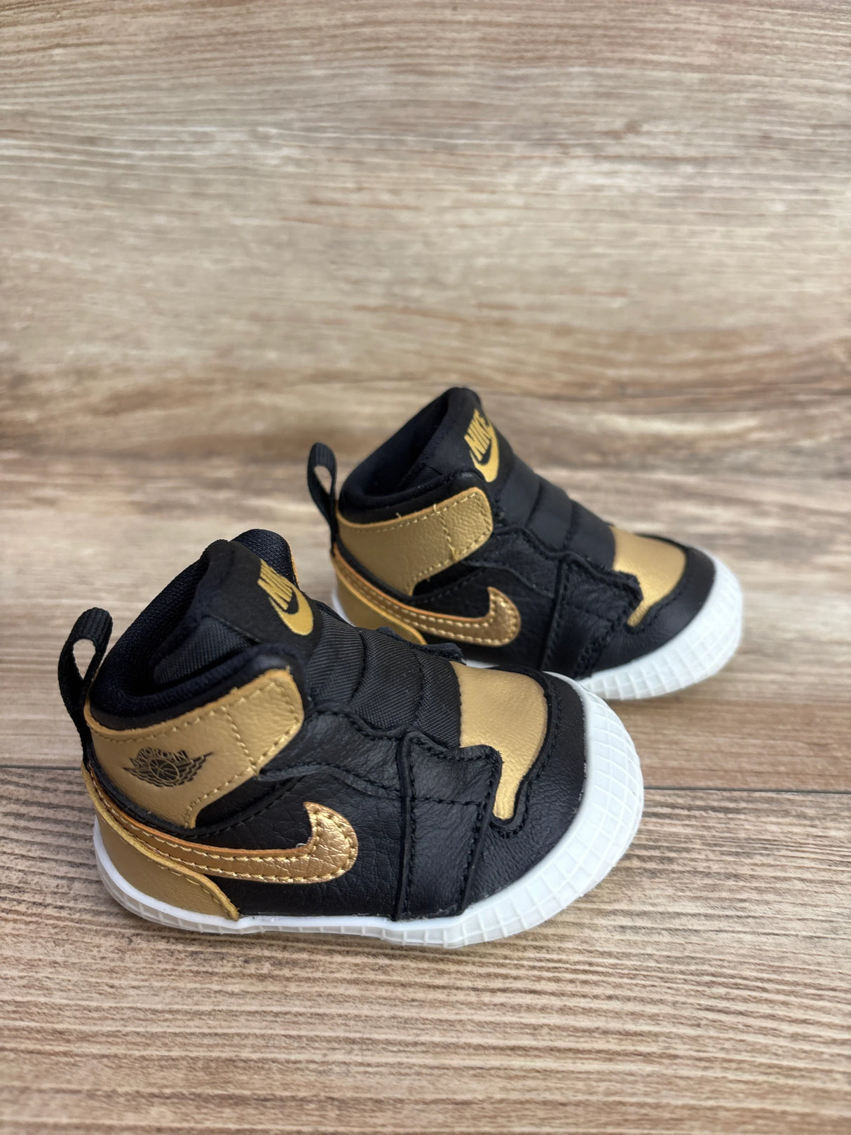 Black and gold toddler Nike basketball sneakers with white soles on wooden surface