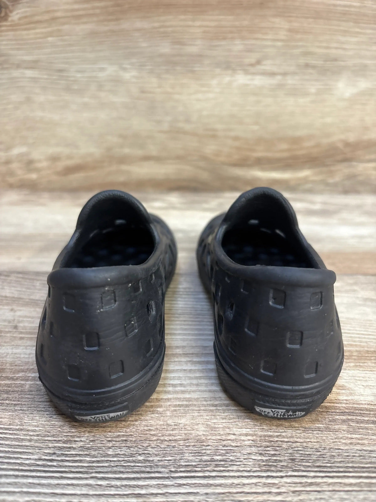 Back view of Vans Slip-On TRK Sandals in black showcasing square cutout pattern and slip-on heel with wood background