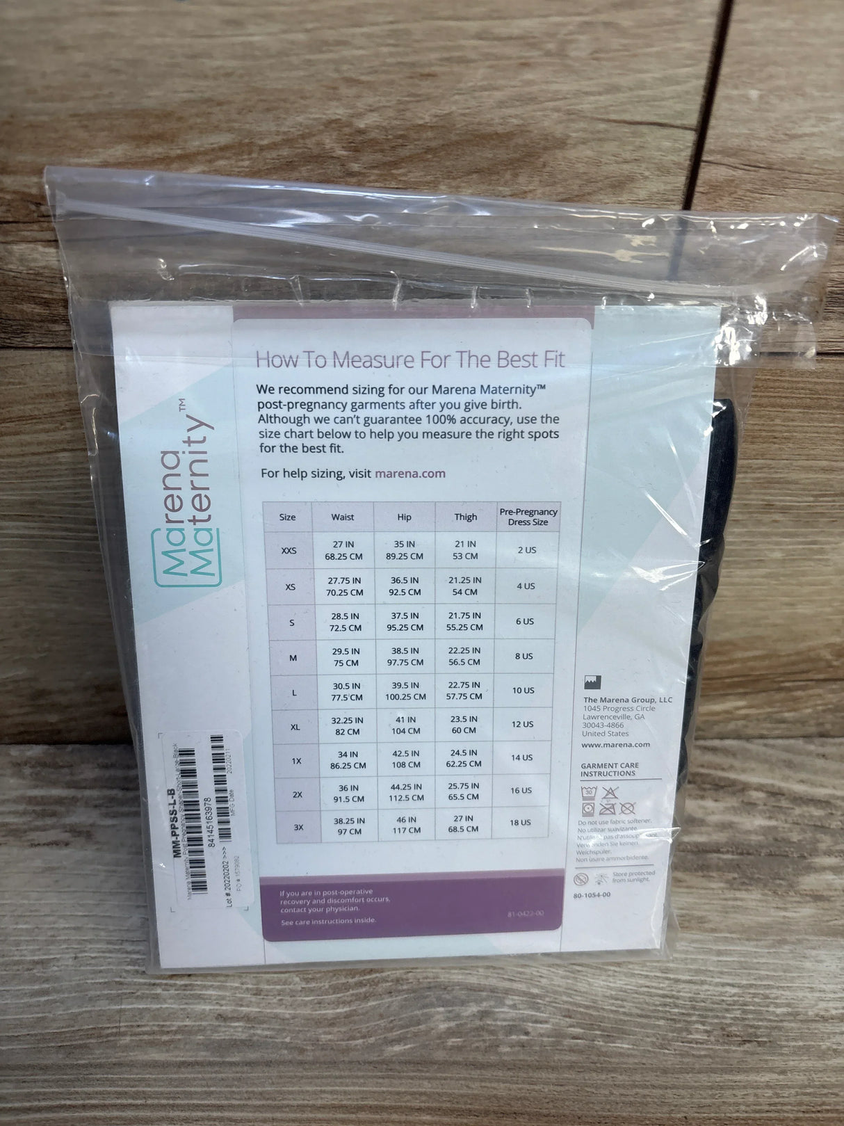 Back view of NWT Marena Maternity post-pregnancy shaper in black in sealed clear packaging with sizing chart on wood plank floor