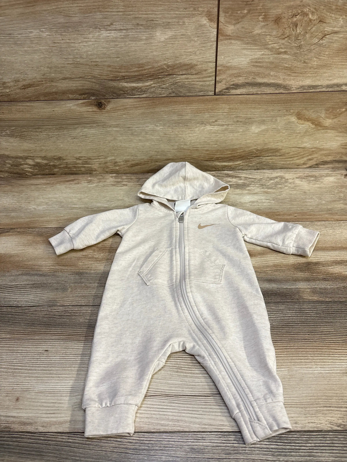 Front view of Nike beige hooded coverall in size 3m, showcasing zip front and pockets on a wood floor