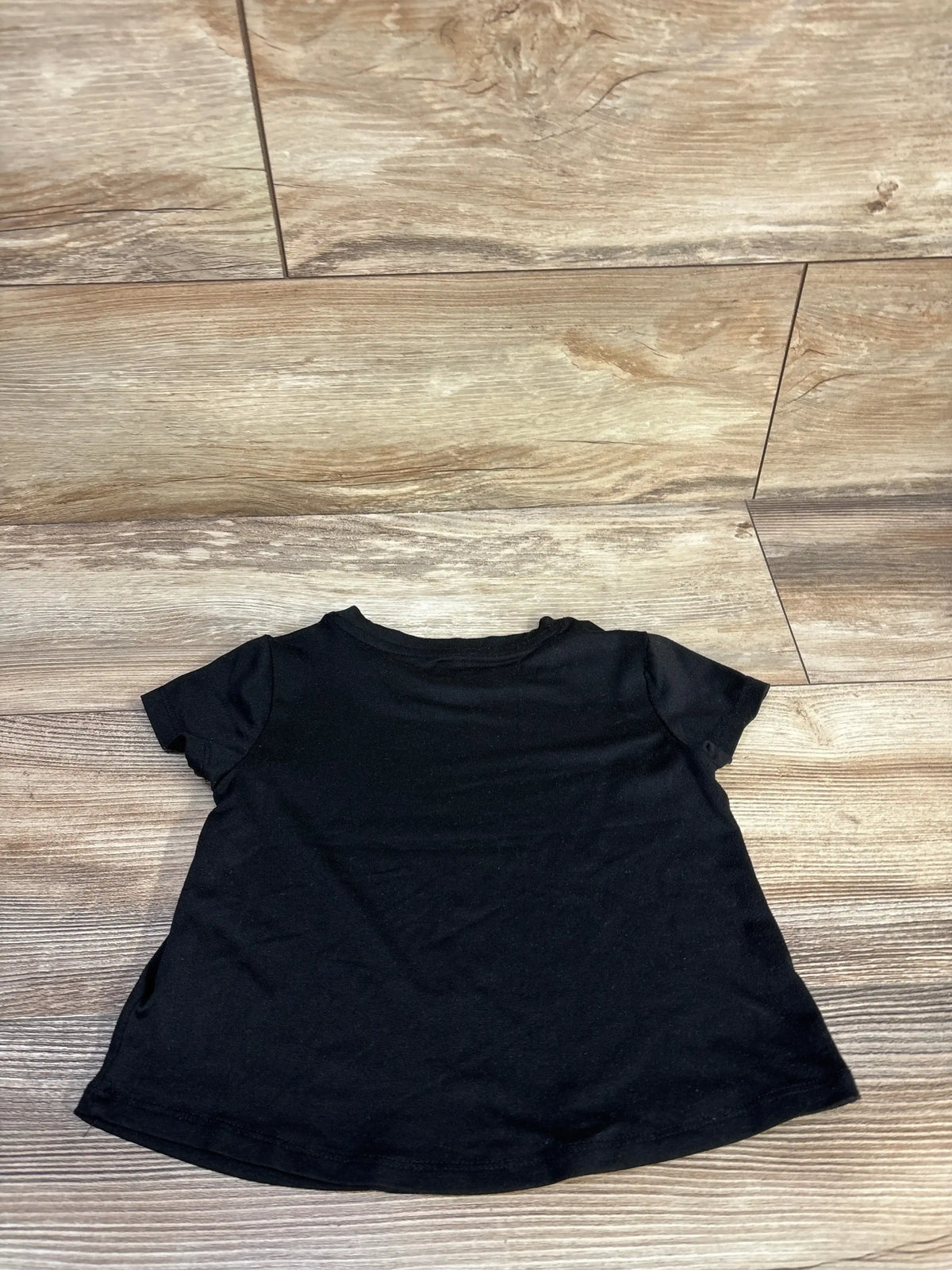 Flat lay of toddler black Ideology Active shirt size 2T showcasing short sleeves and slightly flared hem on light wood floor