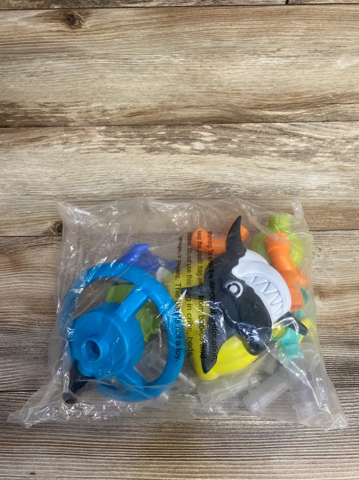 Shark-themed bath toy set with steering wheel in clear plastic packaging on wood background