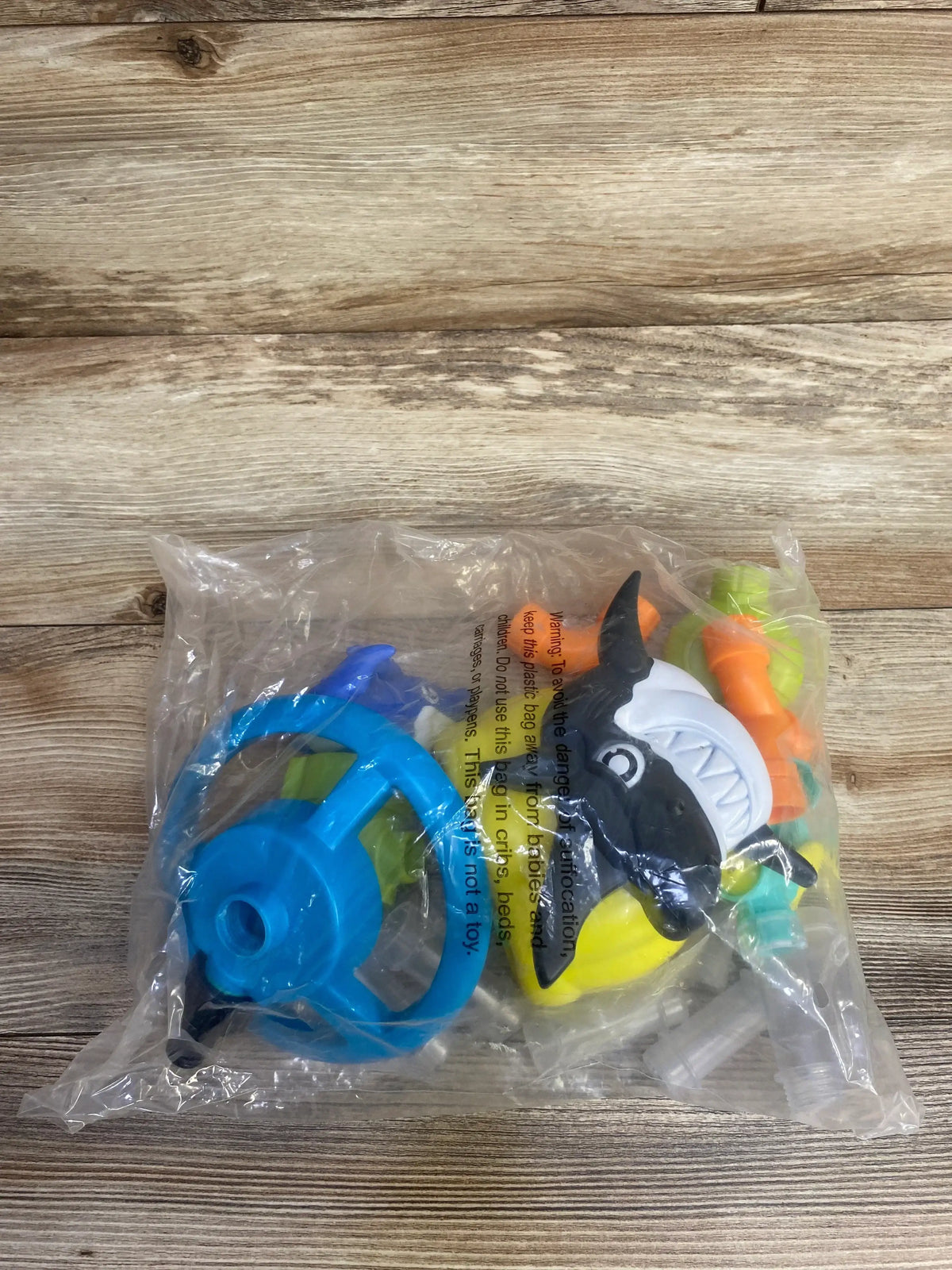 Shark-themed bath toy set with steering wheel in clear plastic packaging on wood background