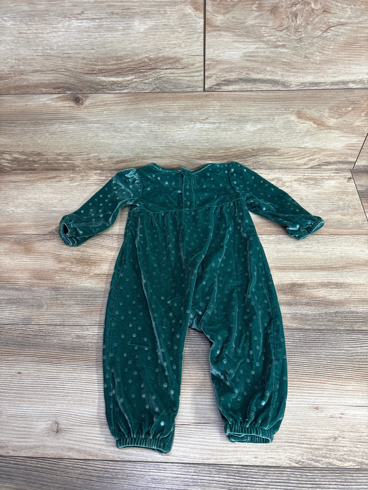 Green velvet long sleeve baby romper with polka dots, flat lay on wooden floor