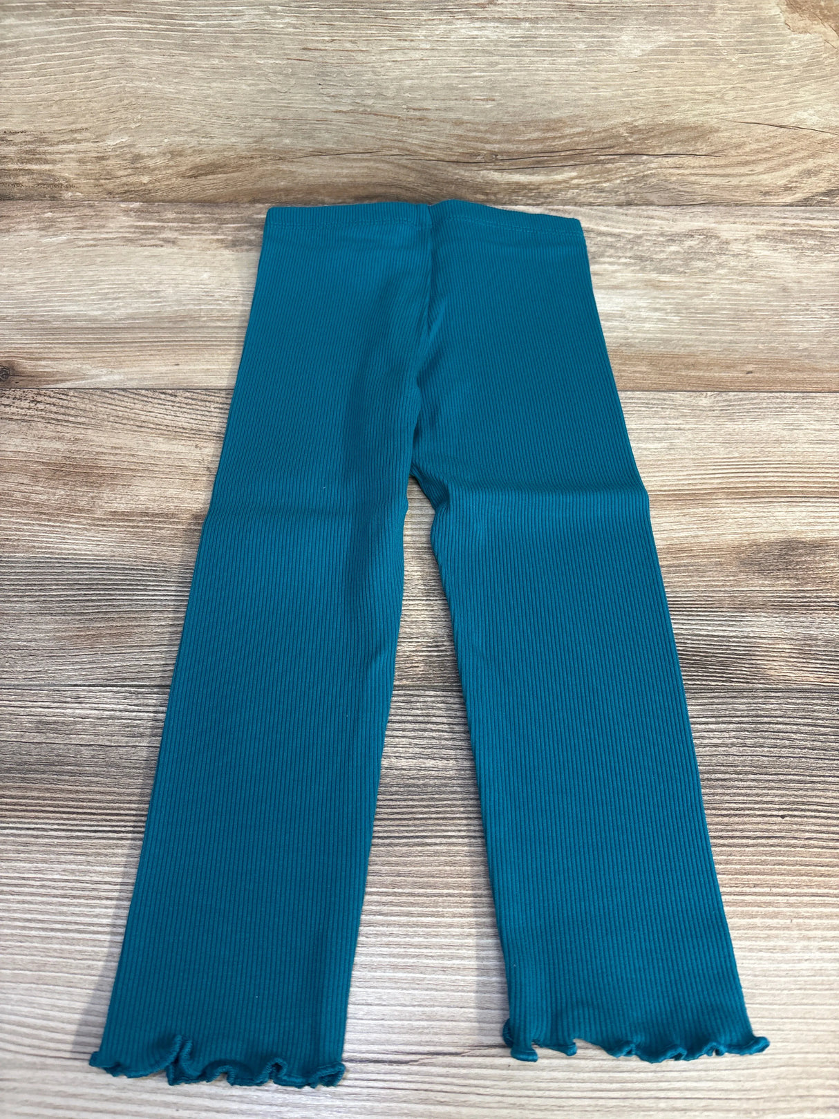 Teal ribbed toddler pants with ruffled cuffs on wooden background