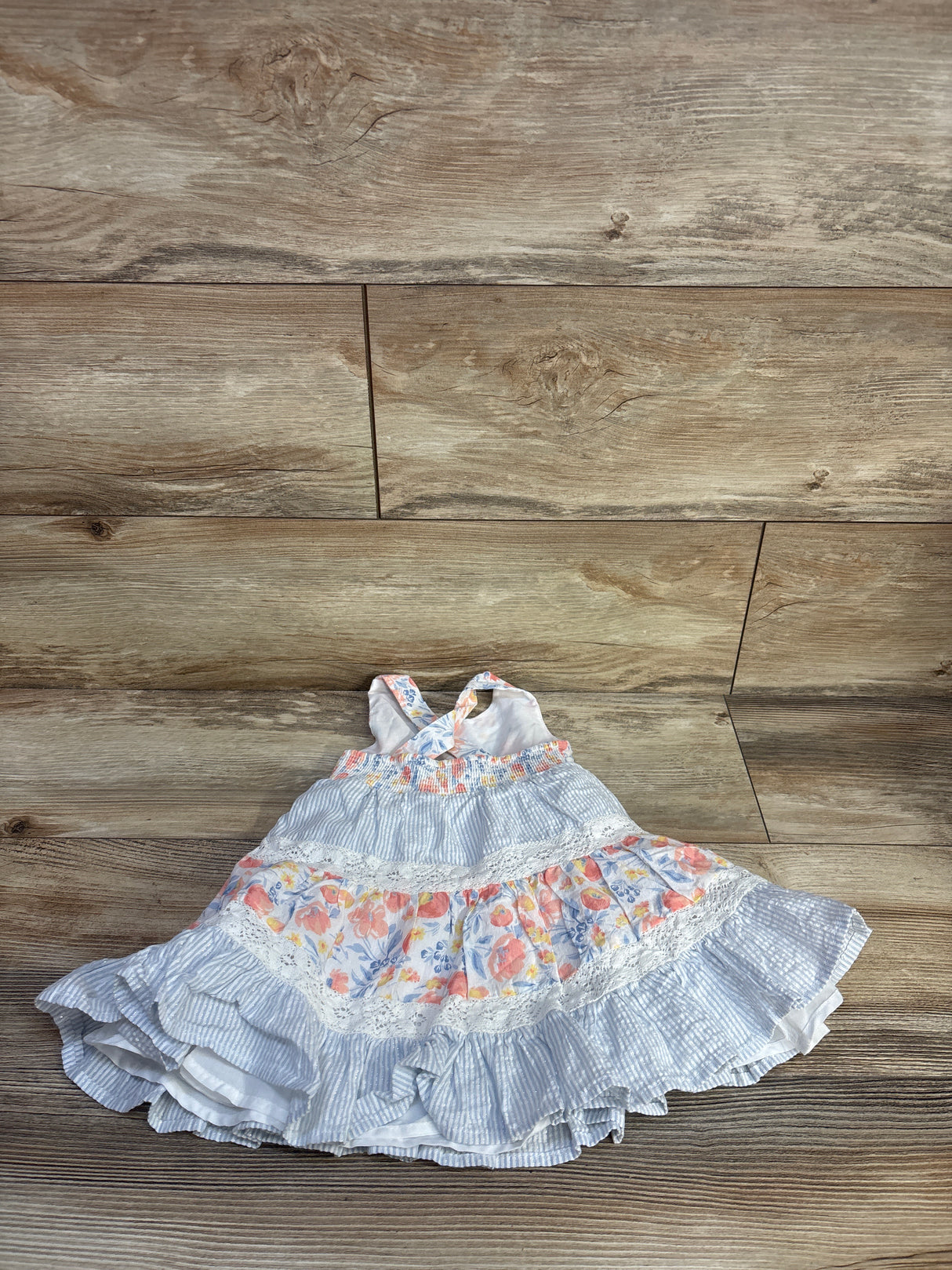 Flat-lay of Tommy Bahama tiered sleeveless dress size 12 months showing floral panels and lace on wood background