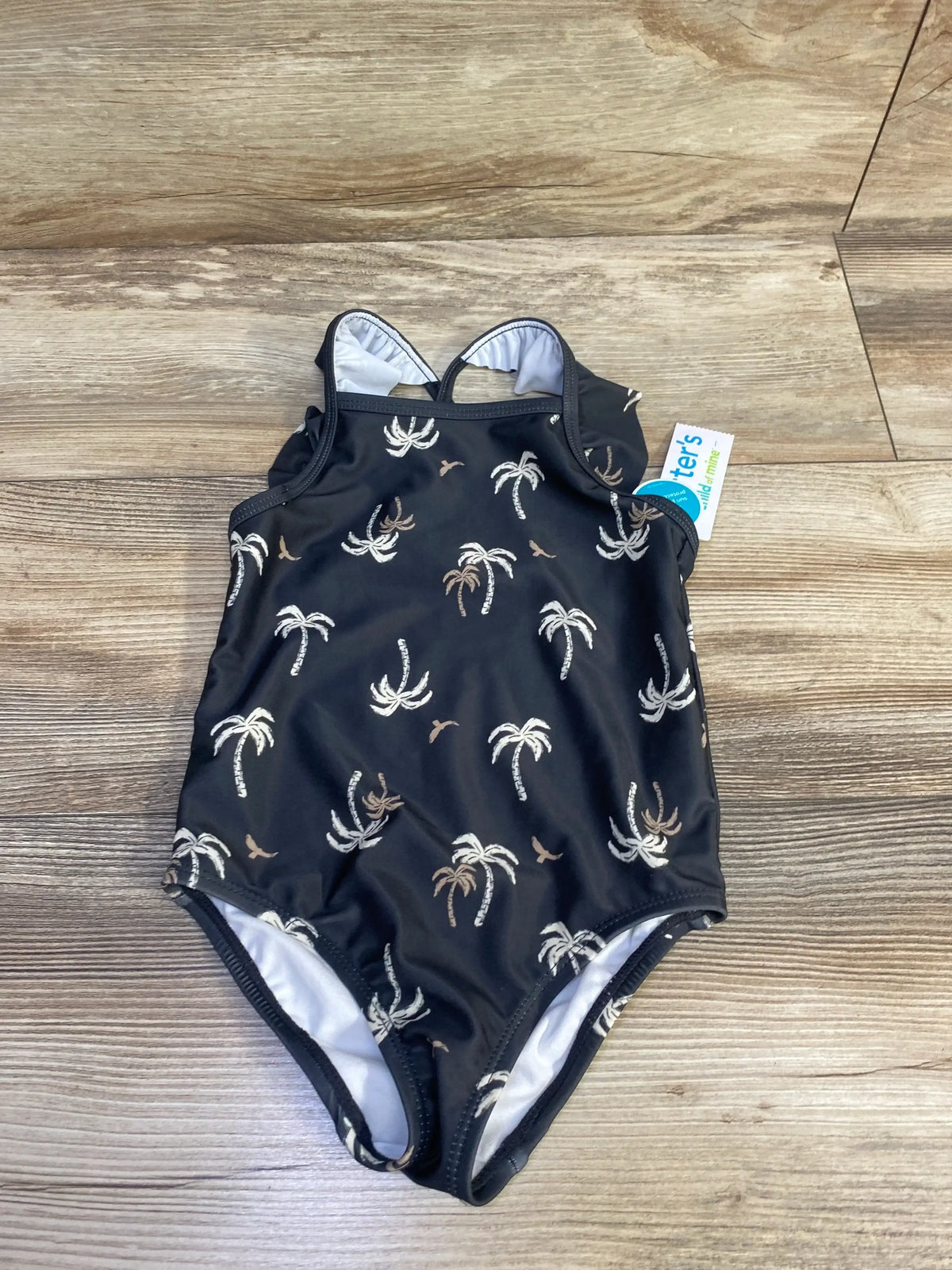 Front view of black Child Of Mine one piece swimsuit, size 4T, with palm tree print on a wood look floor
