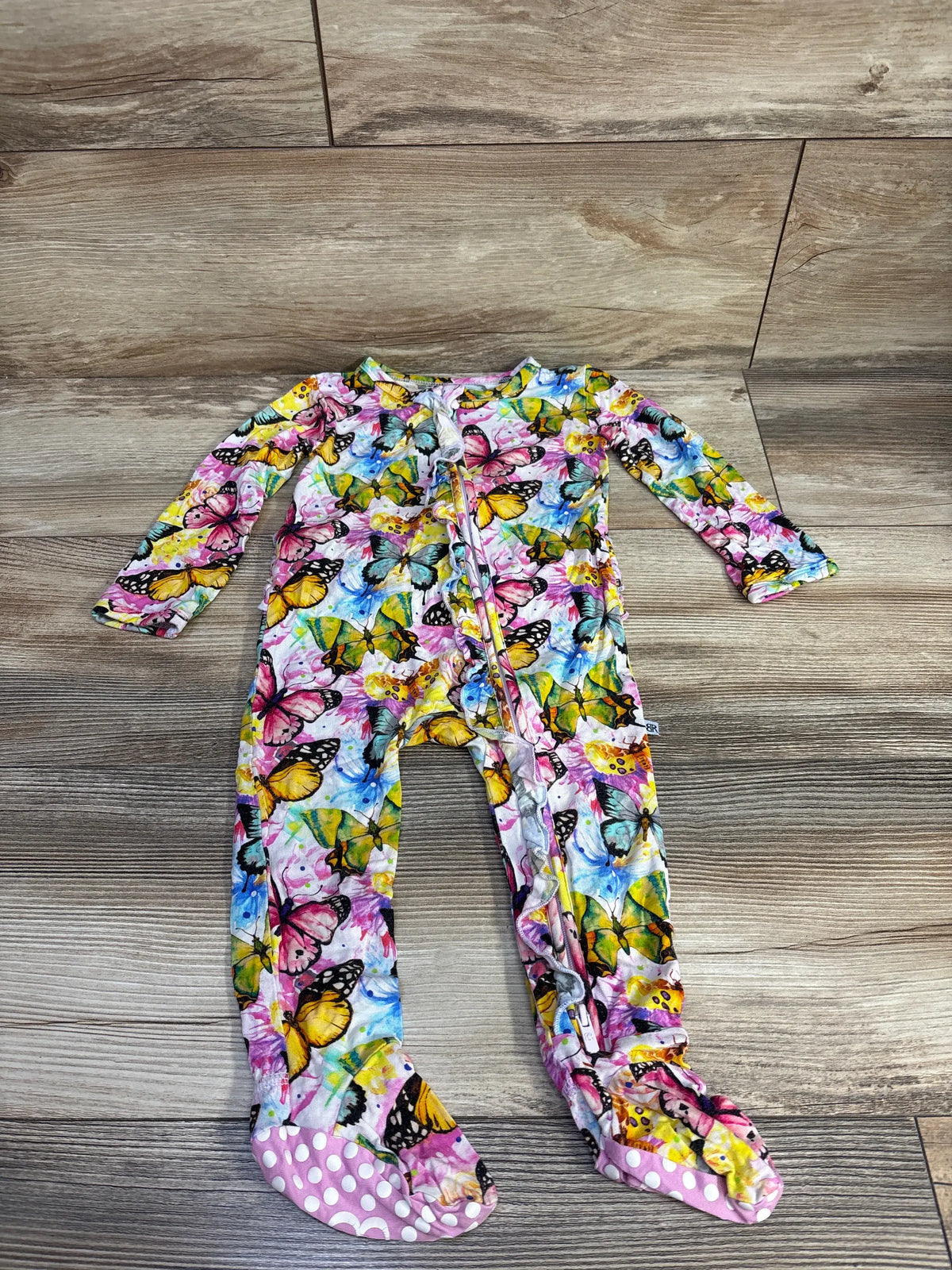 Front view of Bums and Roses butterfly ruffle footie showing white base, colorful butterfly pattern, ruffled trim, and covered feet