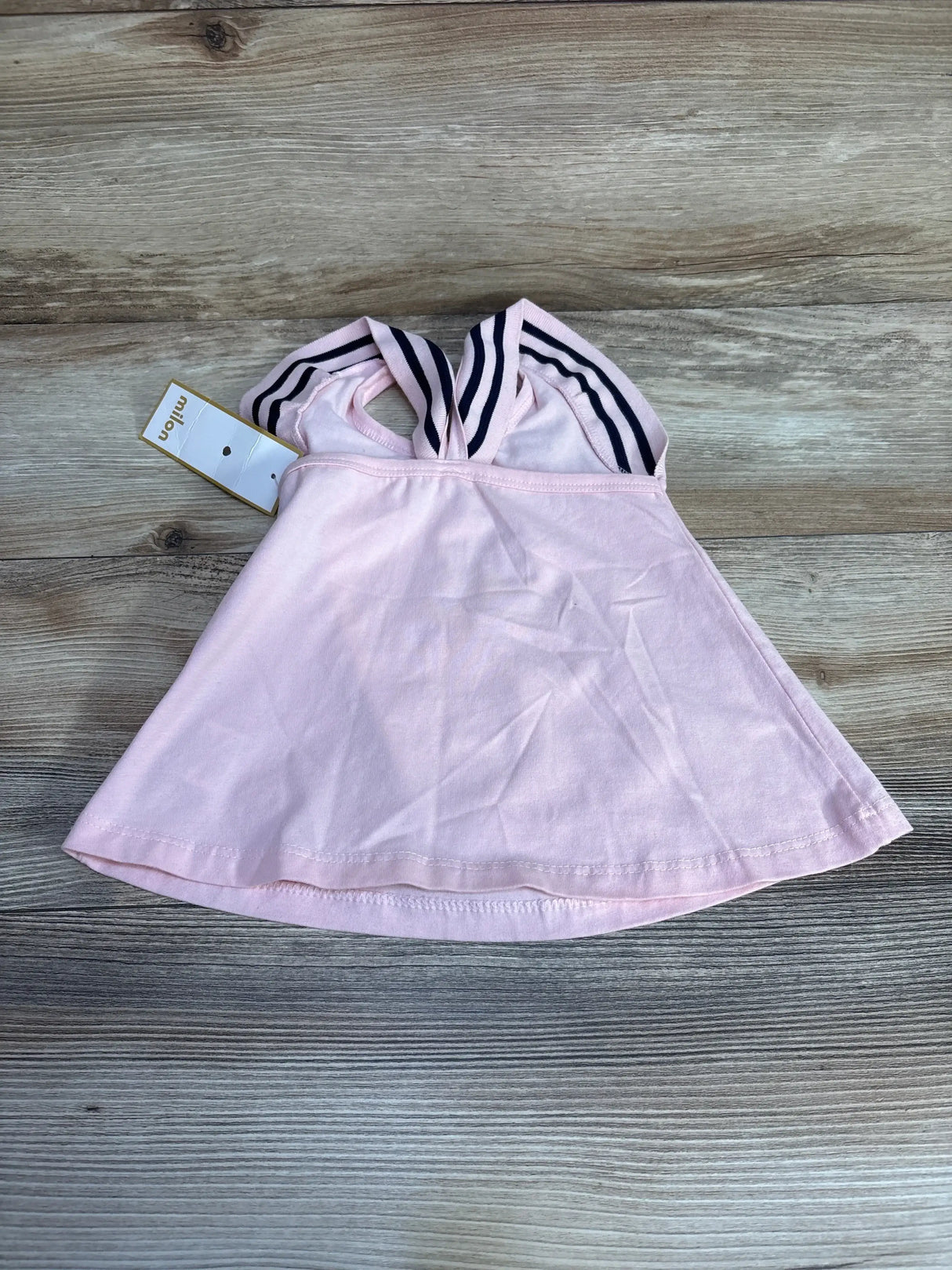 Top down view of pink Milon sleeveless top size 12 months showing navy white striped crossover straps and tag on wood surface