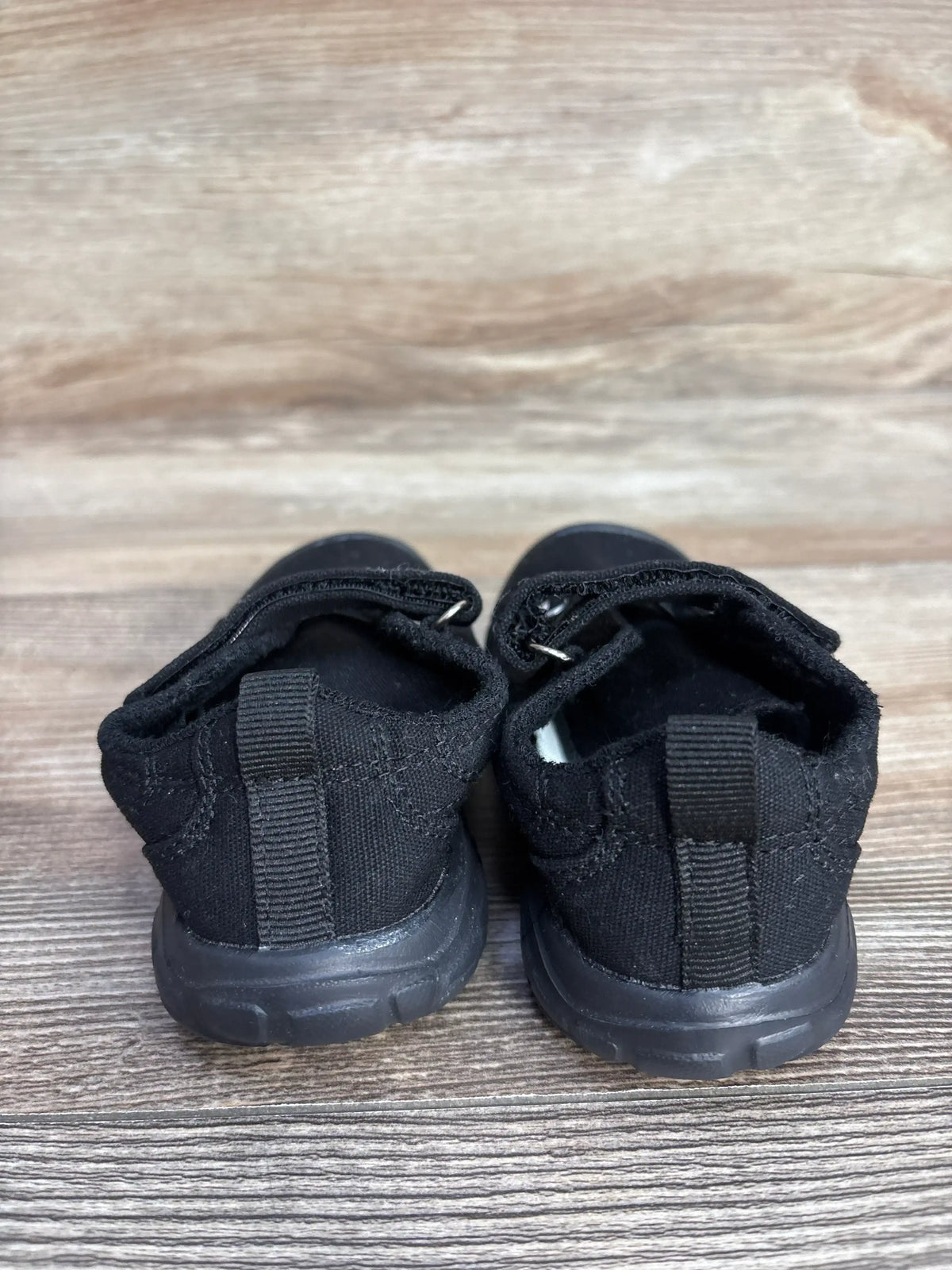 Pair of black toddler shoes with Velcro straps on wooden floor