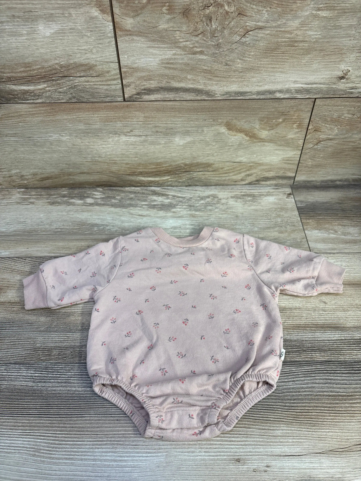 Flat lay of pink sweatshirt bubble romper with tiny floral print, cuffed long sleeves, and elastic leg openings on wood floor