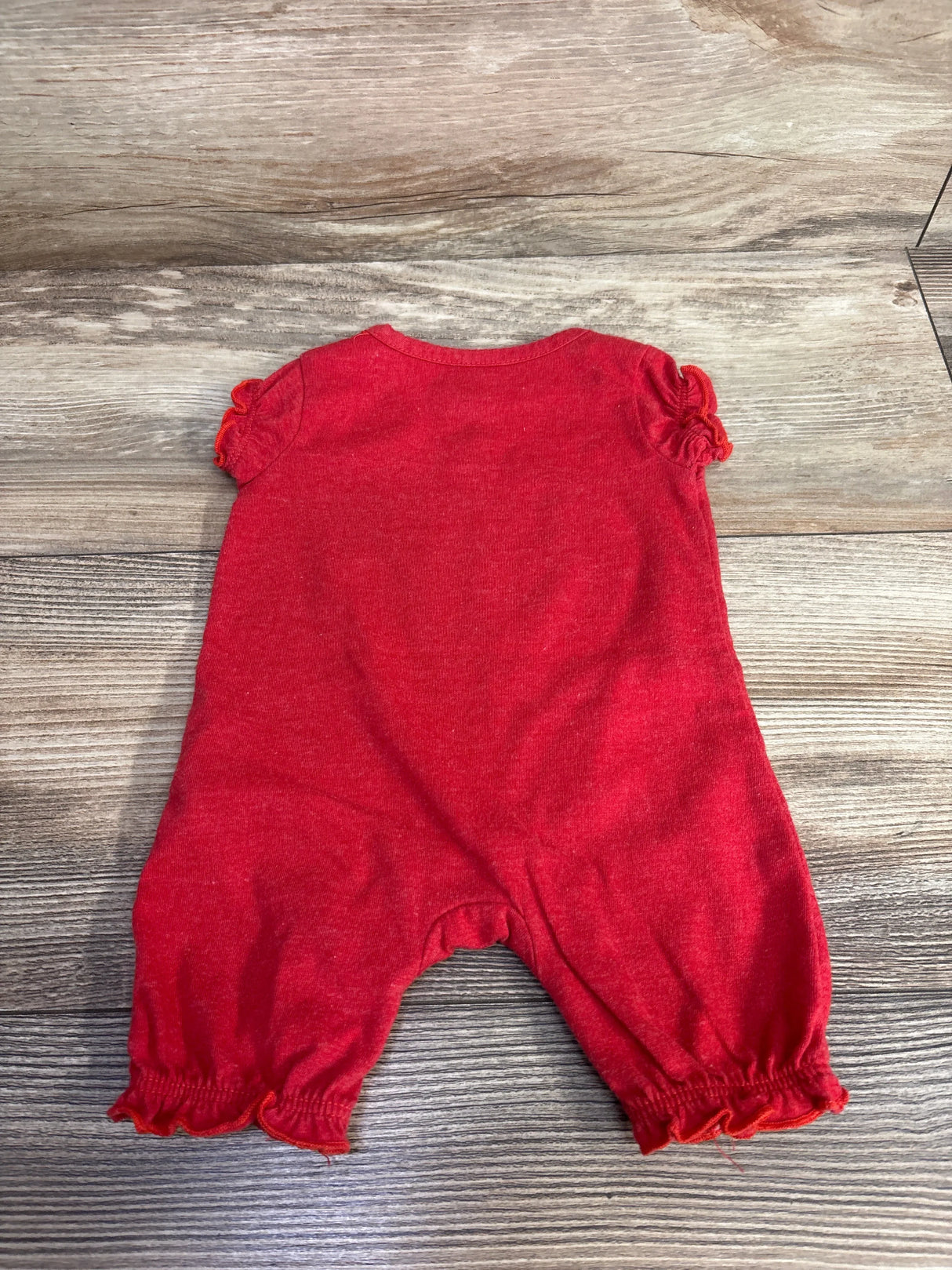 Red short-sleeve baby romper with ruffled edges laid flat on wooden floor background