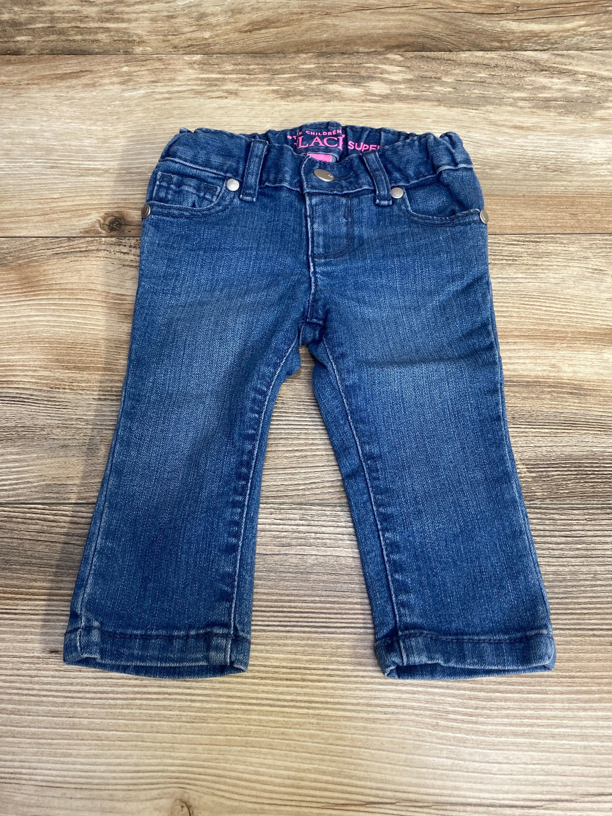 Front flat-lay of Children's Place skinny baby jeans (6-9 months) with elastic waist, faux pockets and cuffed hems on wood