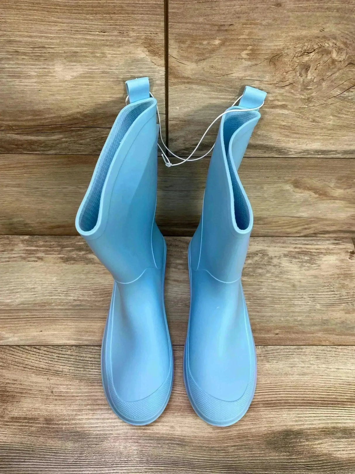 Top-down view of Cat & Jack Andy slip-on rain boots size 6Y showing light blue rubber finish and pull tabs on wood floor