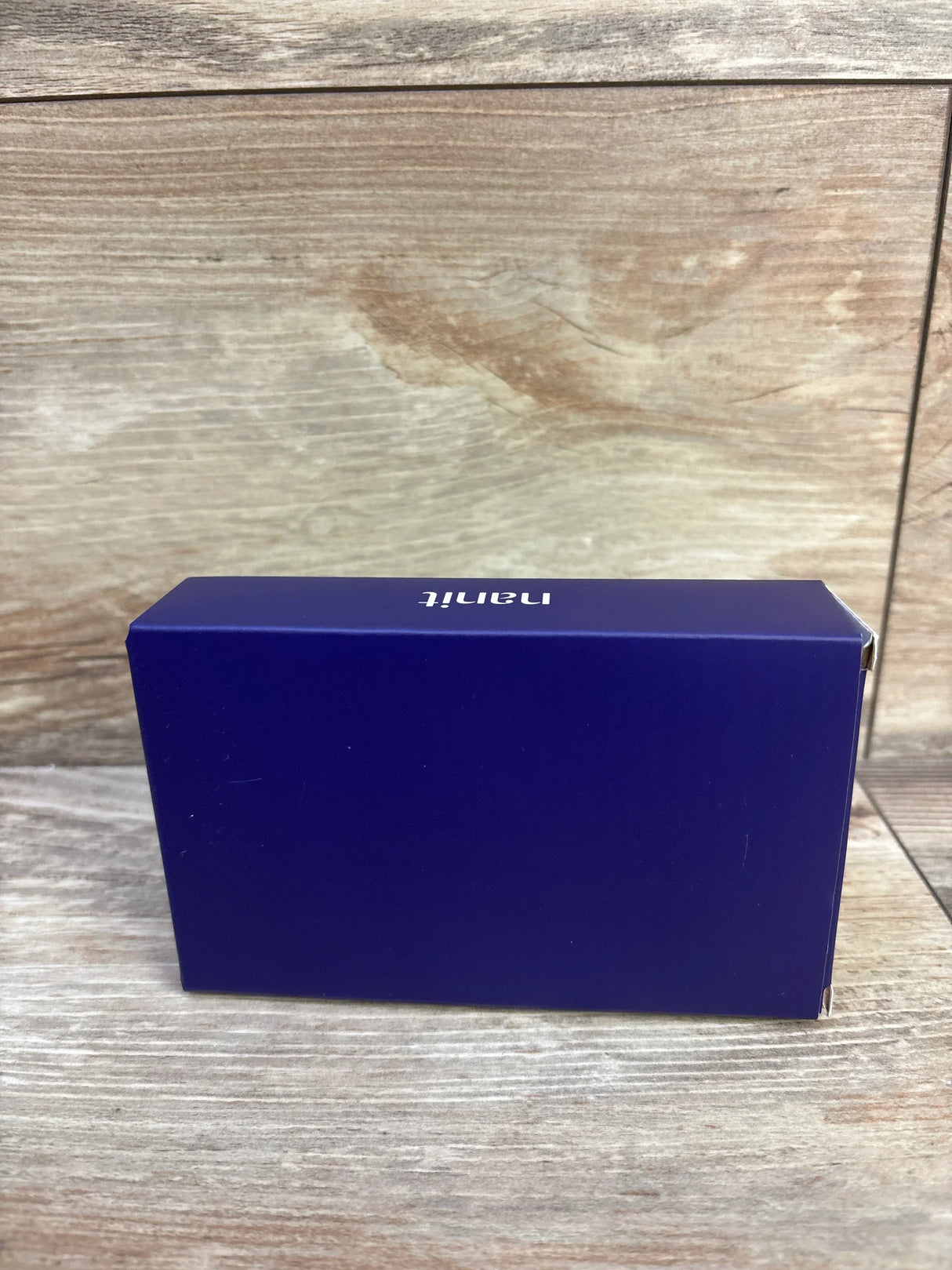 Side view of NEW Nanit Breathing Band sz 0-3m in sealed deep purple Nanit retail box on wood plank floor