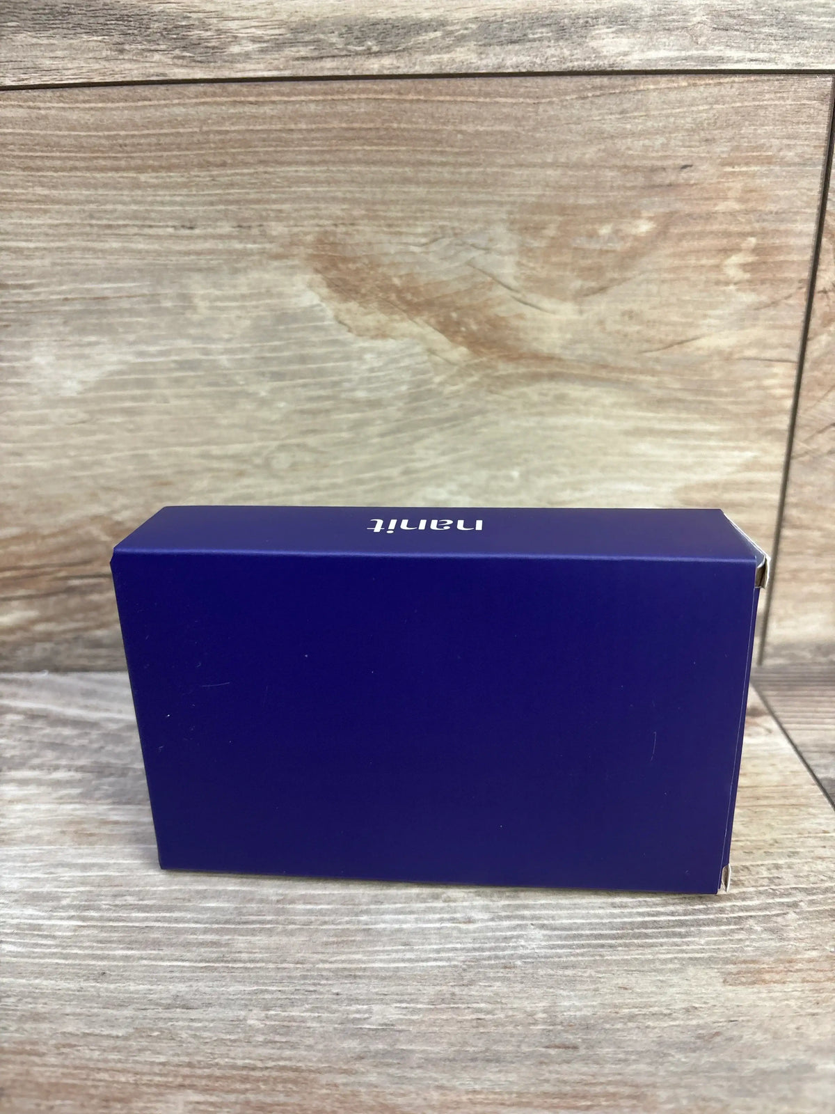 Side view of NEW Nanit Breathing Band sz 0-3m in sealed deep purple Nanit retail box on wood plank floor