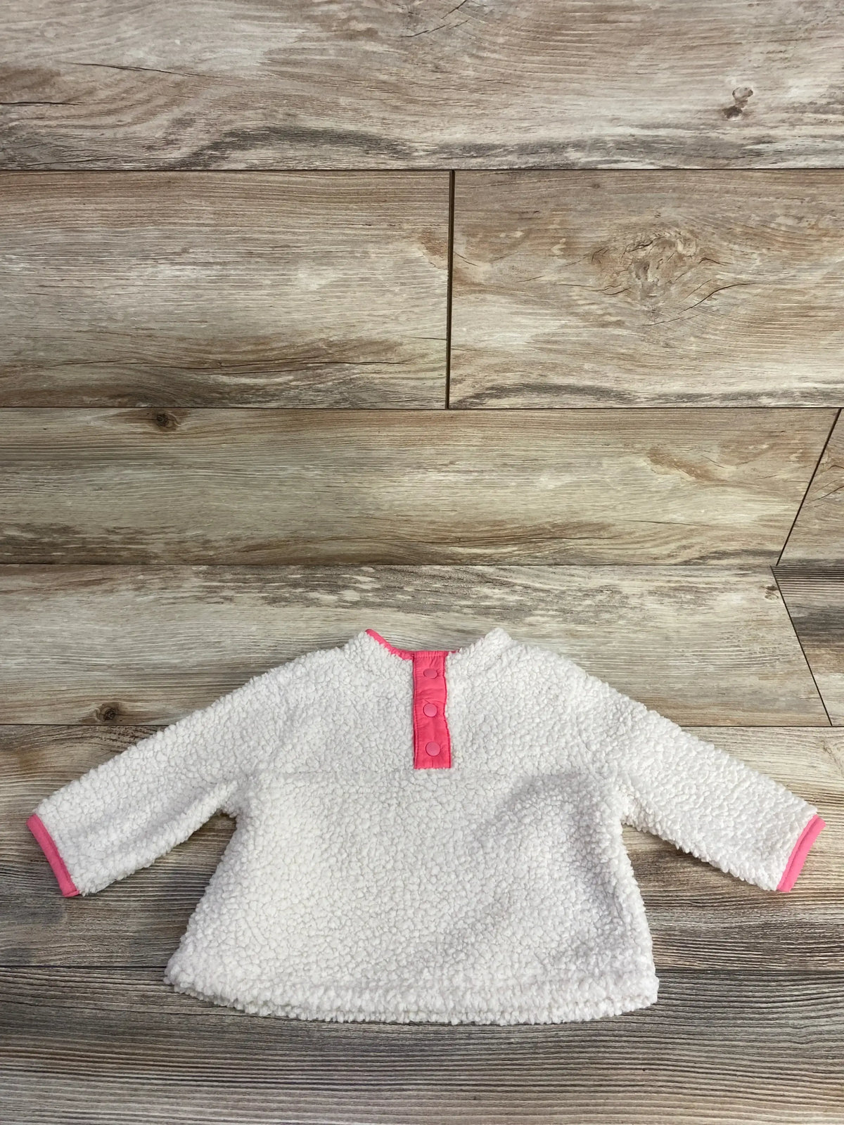 Flat lay of Baby Gap ivory sherpa henley pullover (3–6M) showing pink snap placket and pink cuff trim on wood floor