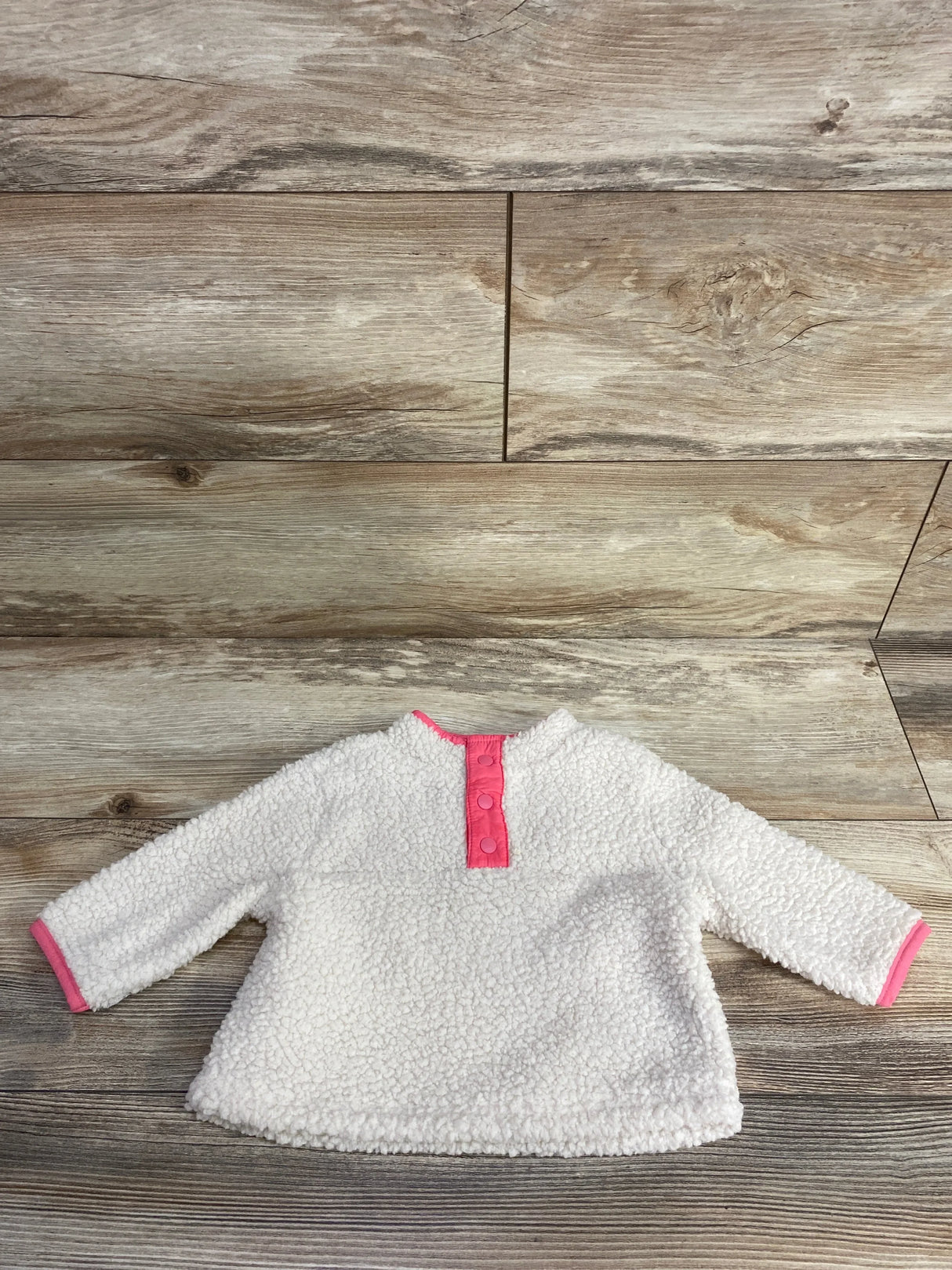 Flat lay of Baby Gap ivory sherpa henley pullover (3–6M) showing pink snap placket and pink cuff trim on wood floor