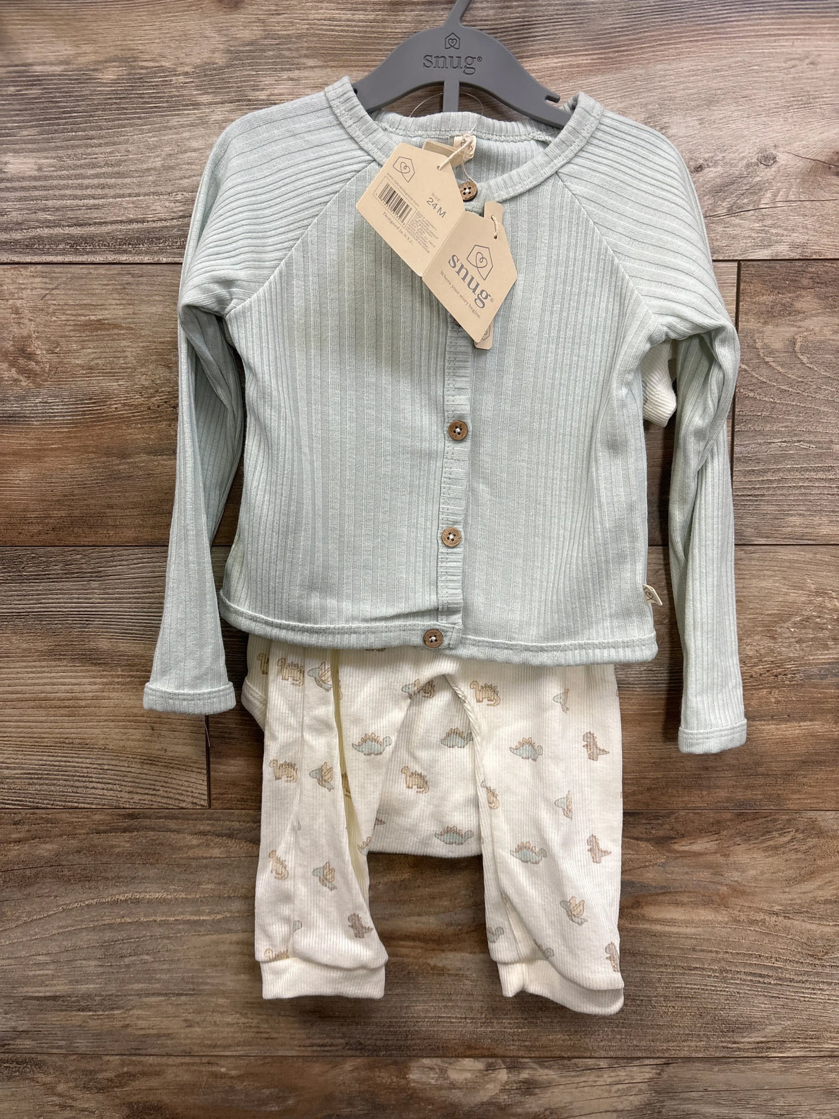 Front view of baby outfit on hanger showcasing light green ribbed cardigan with wood buttons and cream pants with animal print on wood plank floor