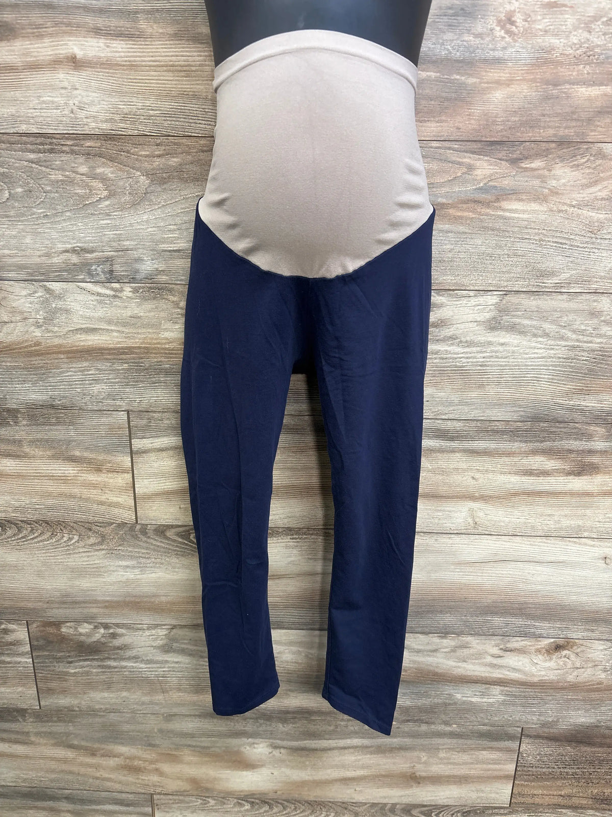 Front view of Motherhood Maternity full panel leggings showcasing navy fabric and beige belly panel with wood plank background