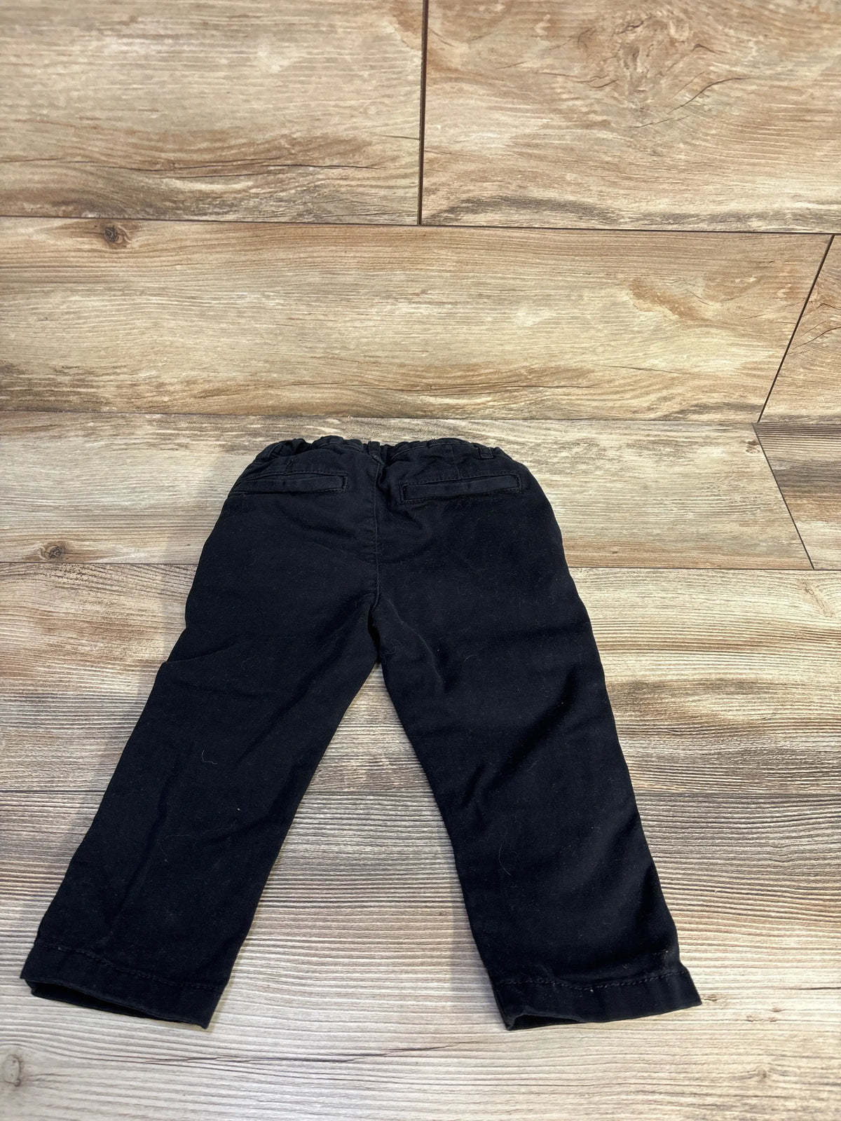 Back view of Children’s Place black pants in size 18 to 24 months showcasing two back pockets on a wood-look floor