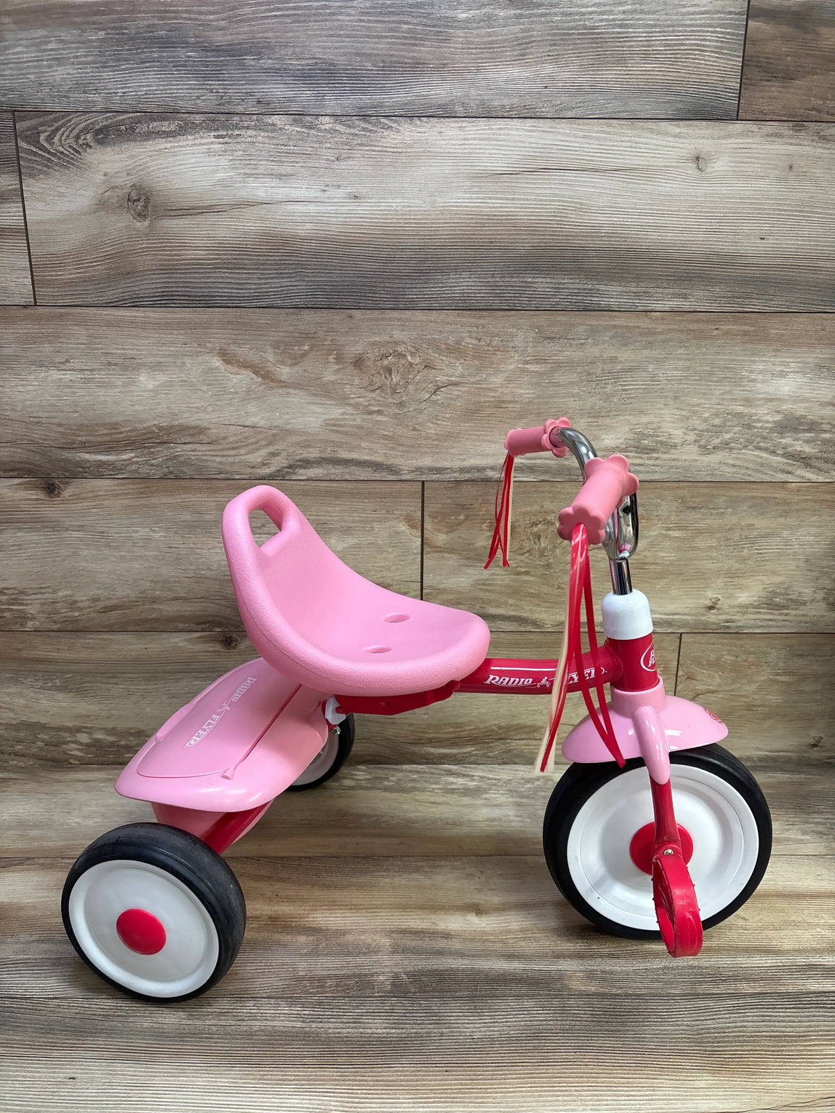 Front three quarter view of pink Radio Flyer Ready to Ride Folding Trike showing three wheels and rear platform on wood floor